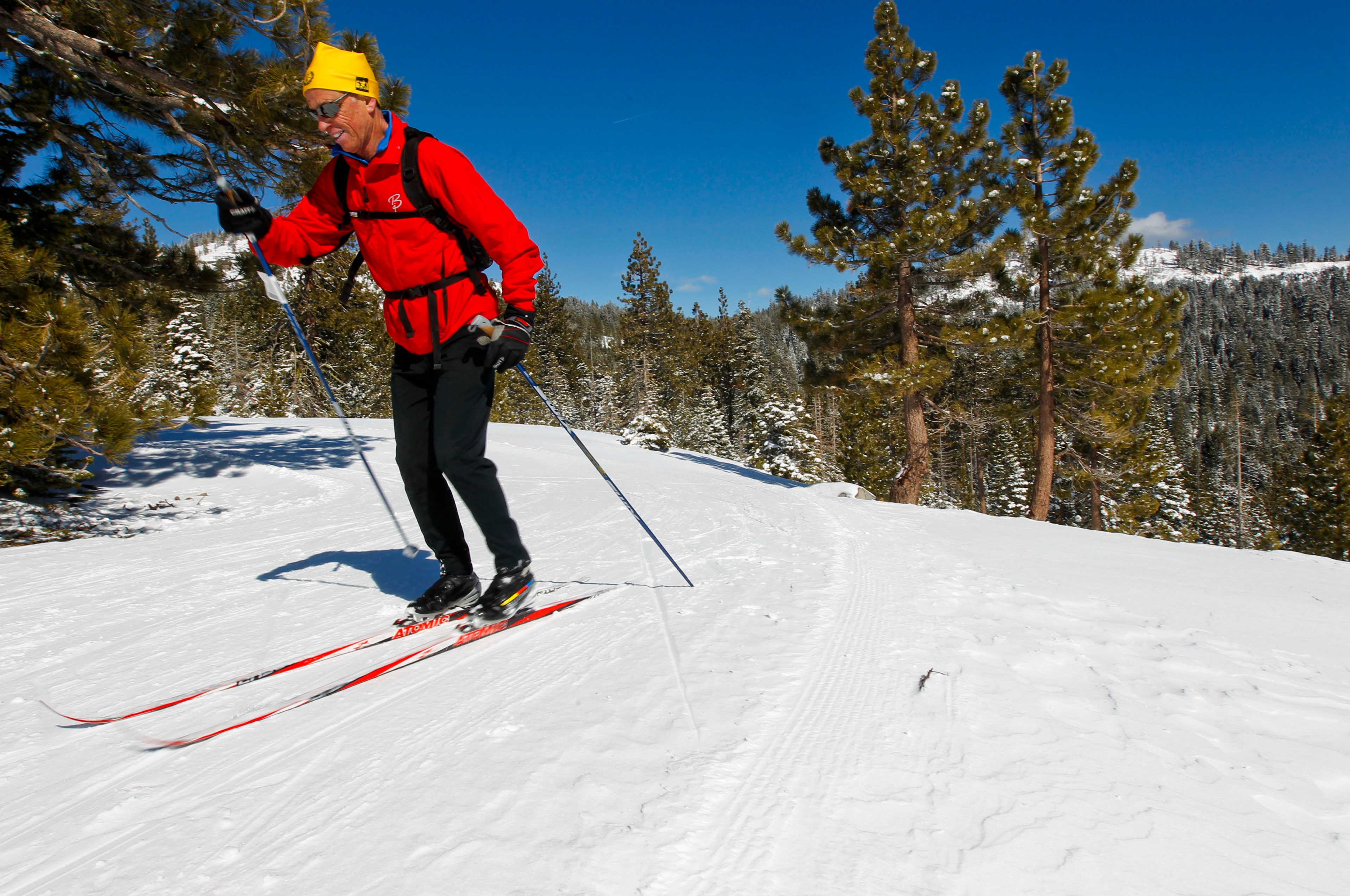 A man in a red jacket cross-country skis with a smile on his face