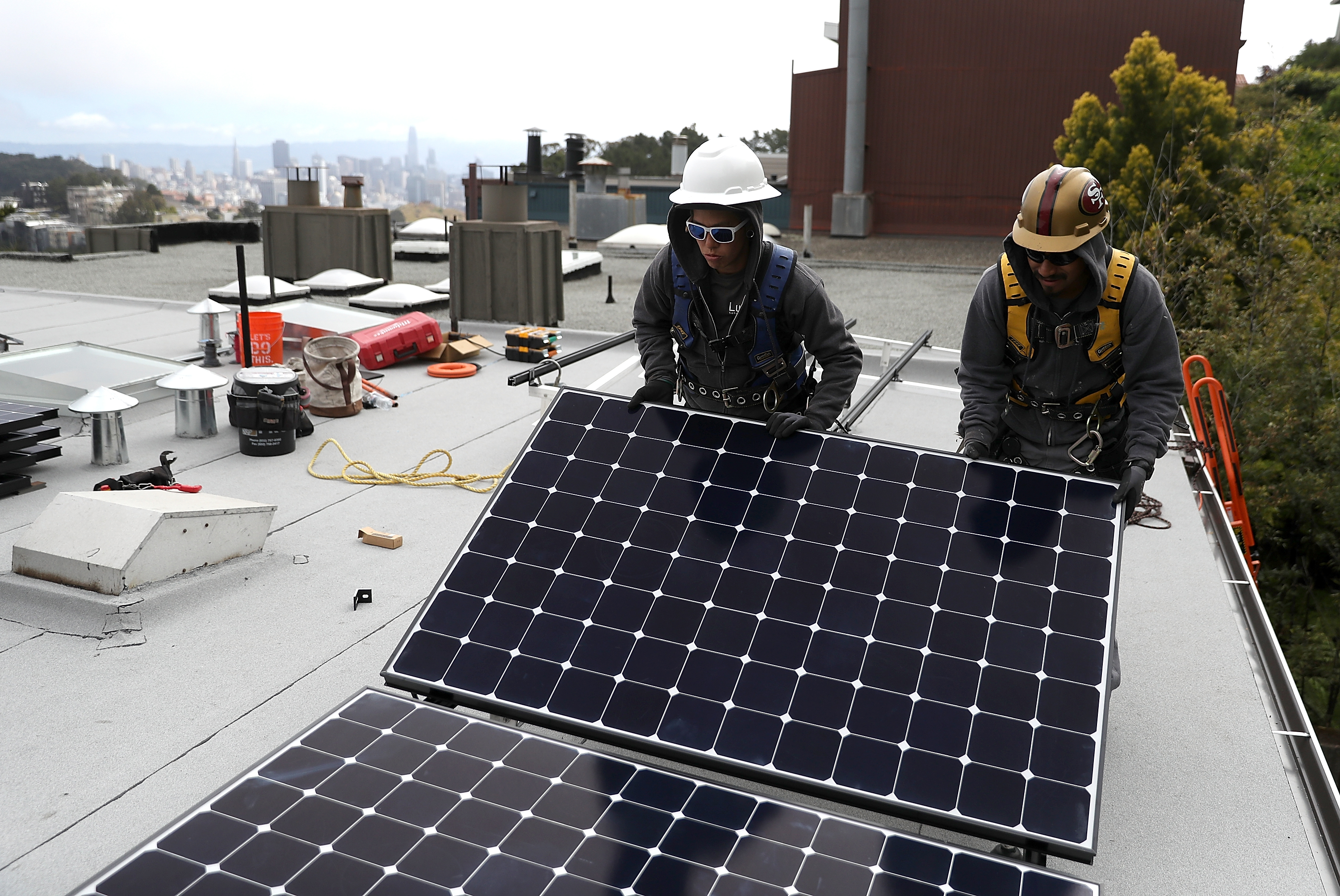 Two workers in hard hats lift solar panel on top of roof