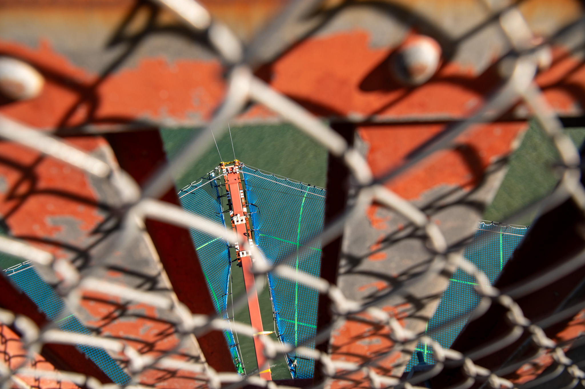 A net is seen through a chain link fence off of a red bridge