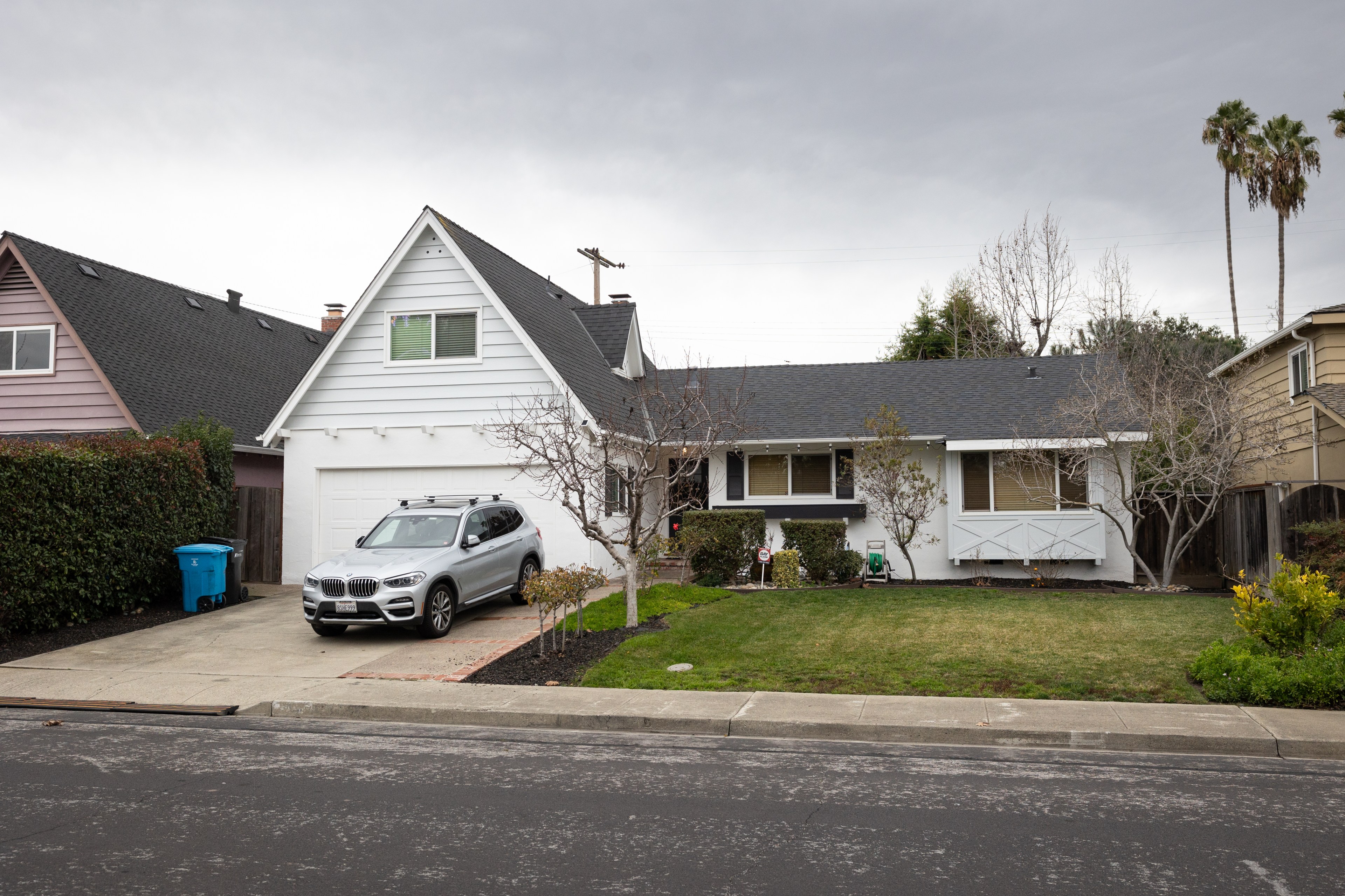 A suburban house with a white garage, driveway, and an SUV parked outside, under overcast skies.