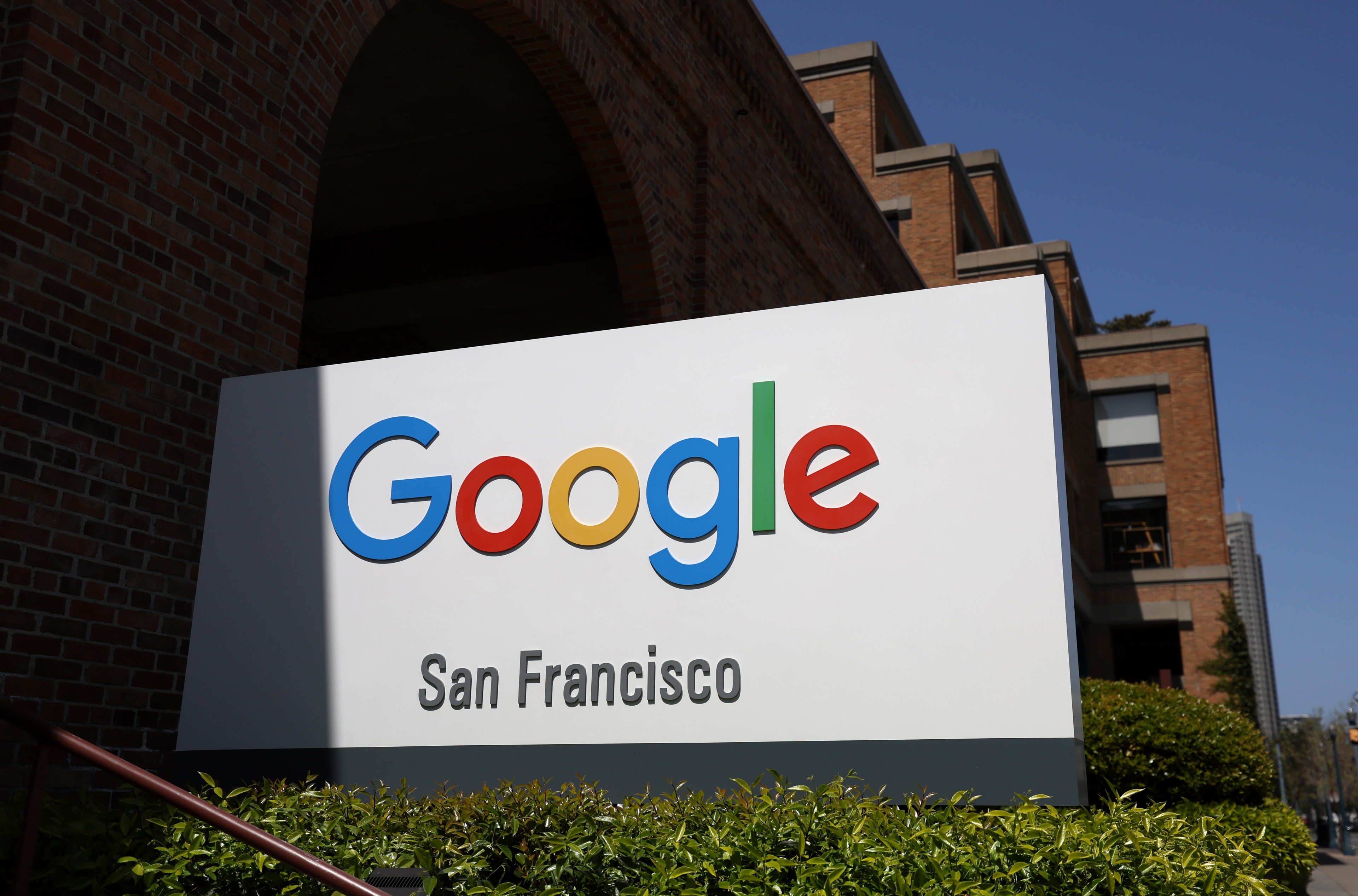 A Google sign with "San Francisco" below, in front of a brick building with arches and greenery.