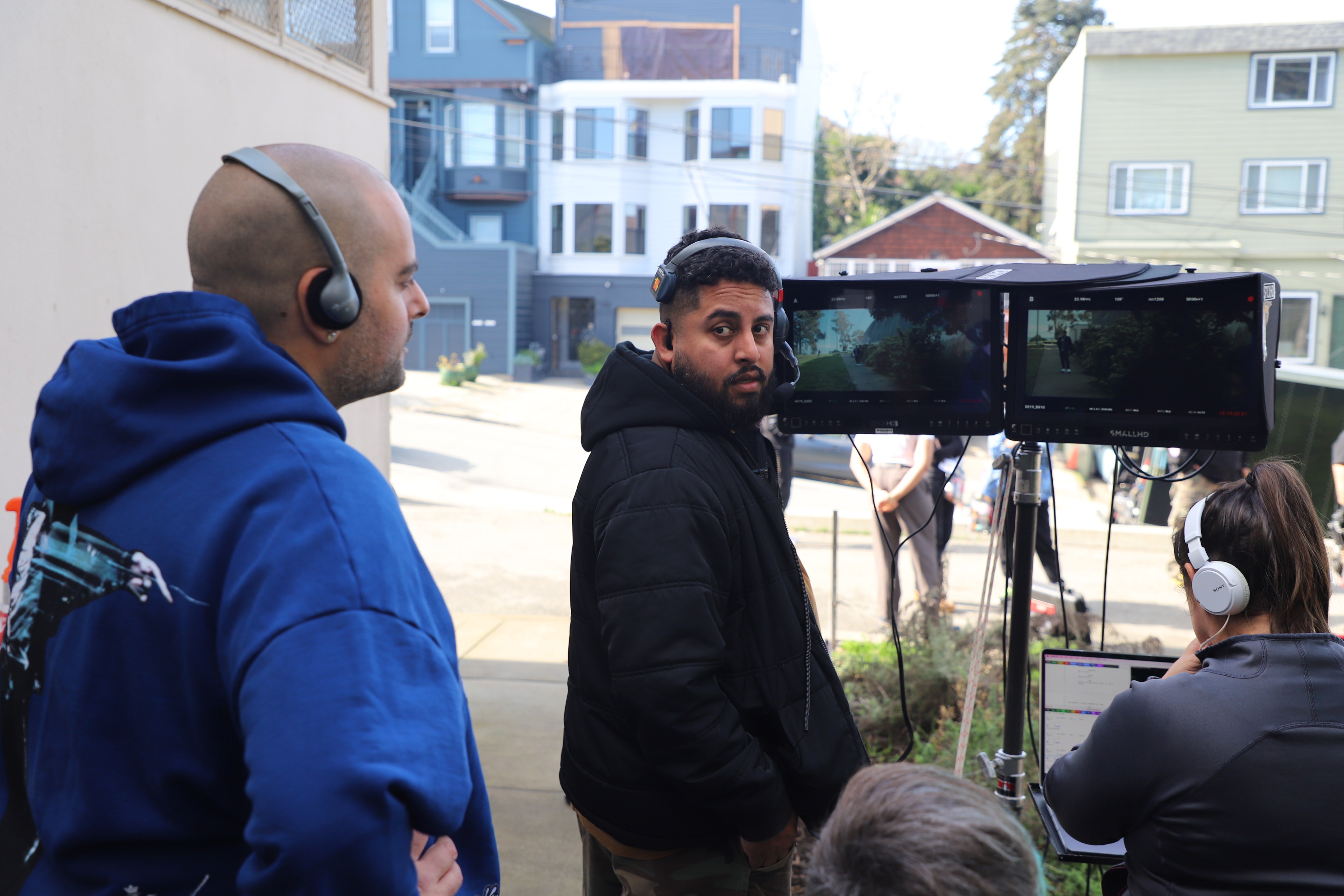 Three people in headphones monitor film production on dual screens with a residential backdrop.