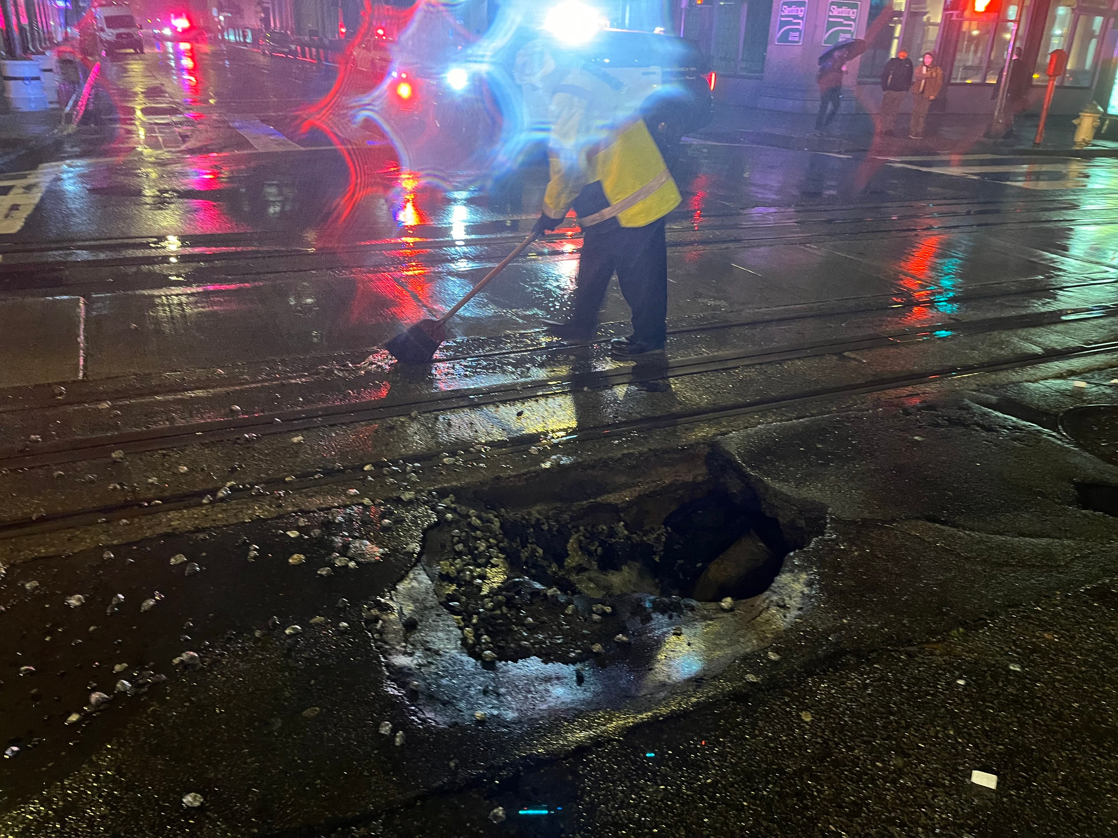 A worker uses a broom to brush water on a cable car track next to a sinkhole