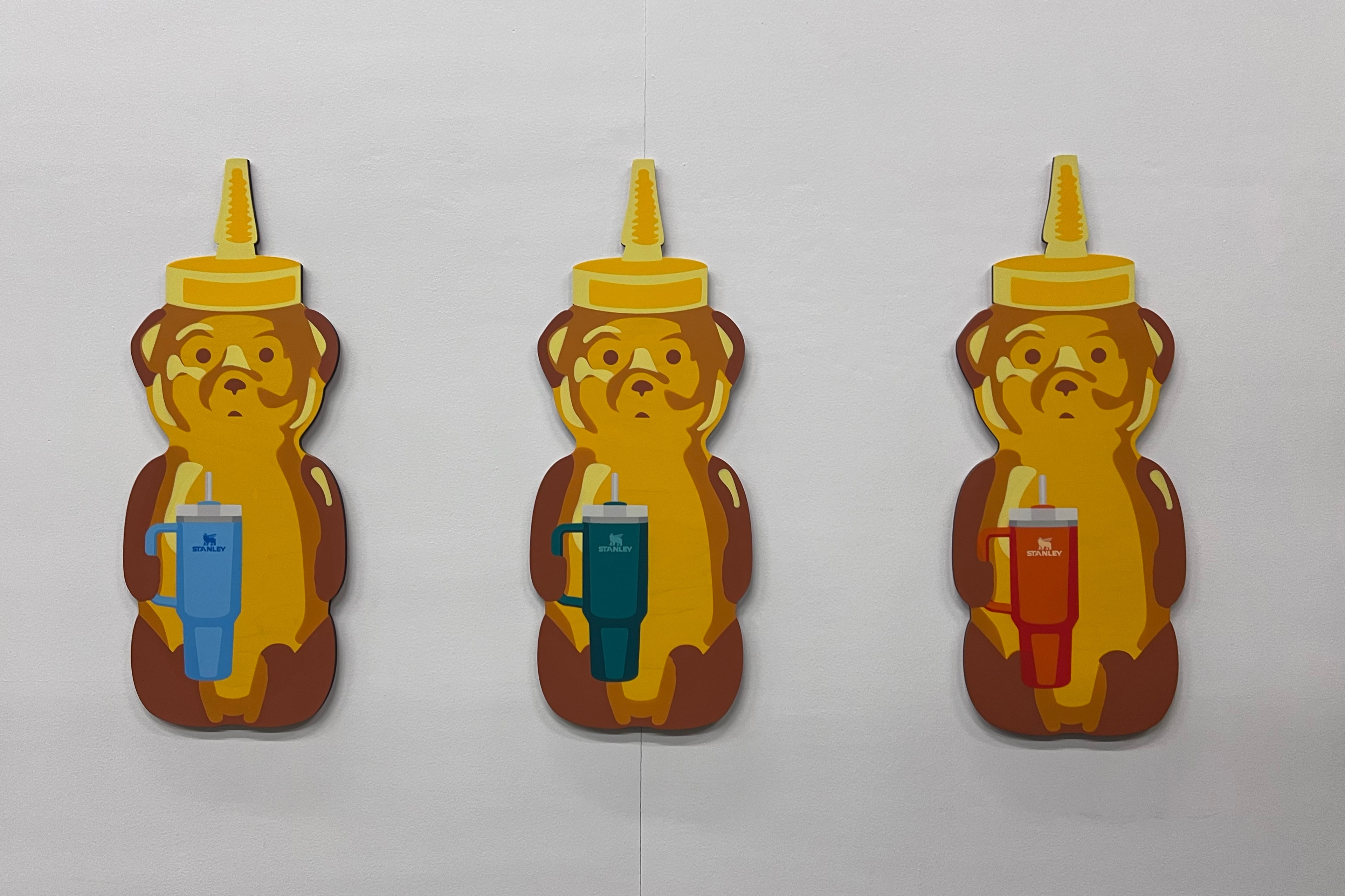 Three cartoon bear-shaped honey bottles with lids on a wall, each holding a different Stanley cup.