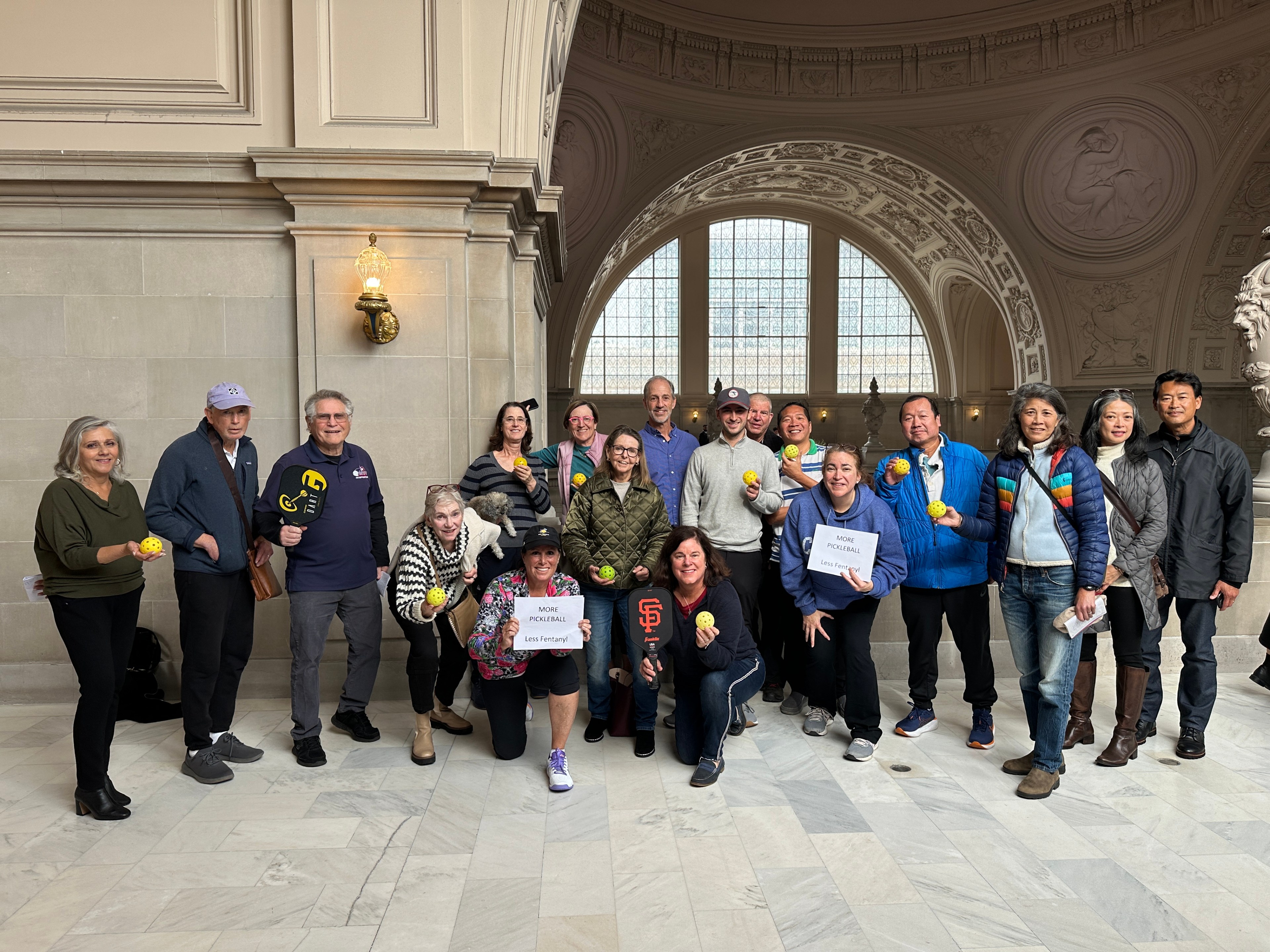 A group of pickleball players poses for a group photo inside San Francisco City Hall. 