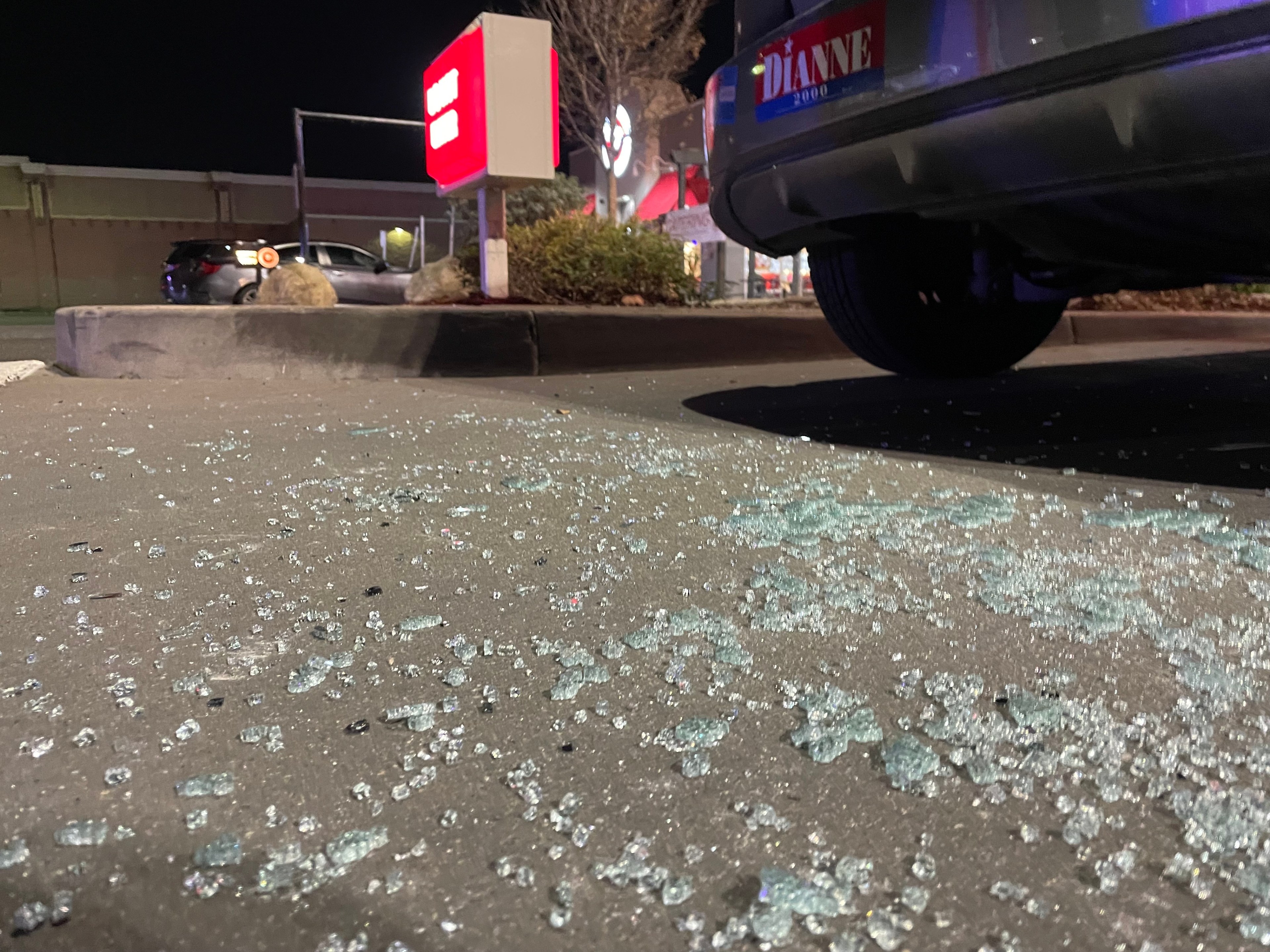 Smashed glass litters the pavement near a parked car.