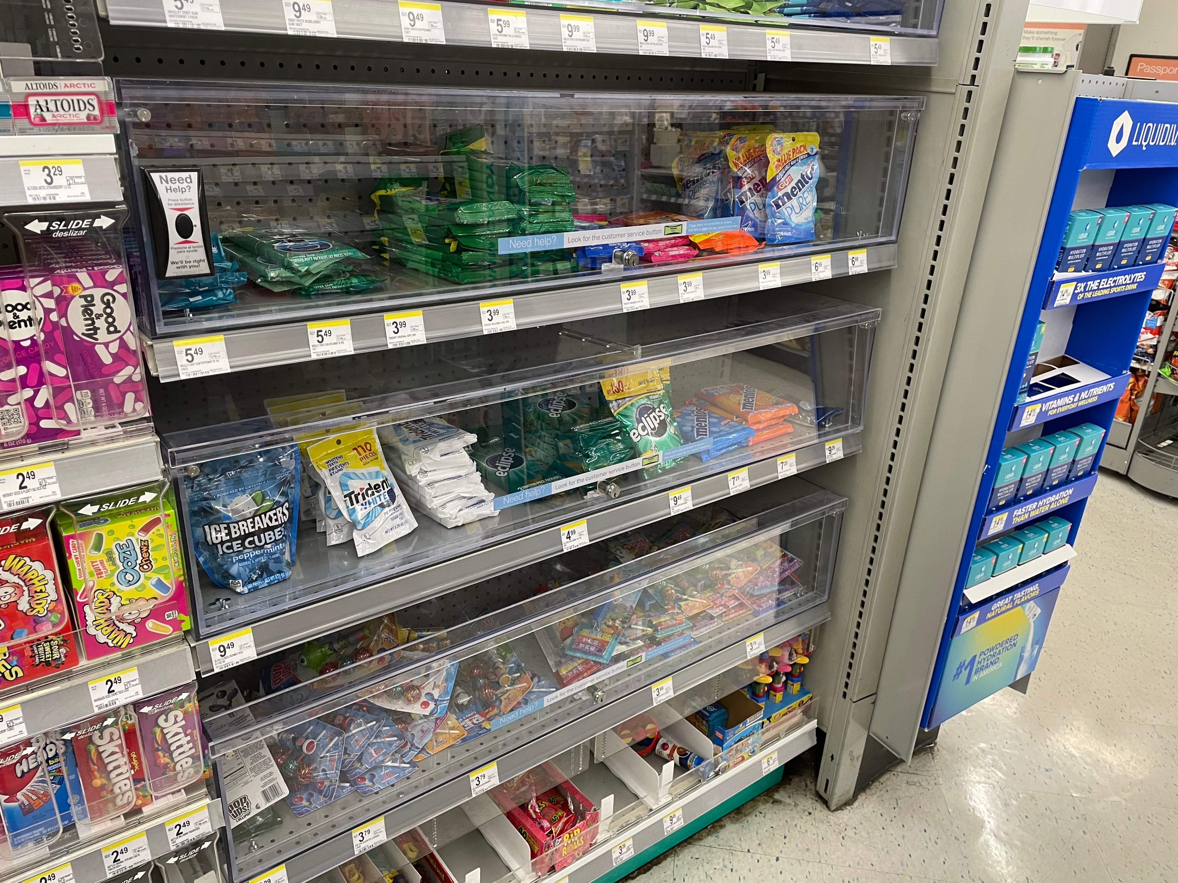 Bags of gum stand locked behind plexiglass at a drug store.