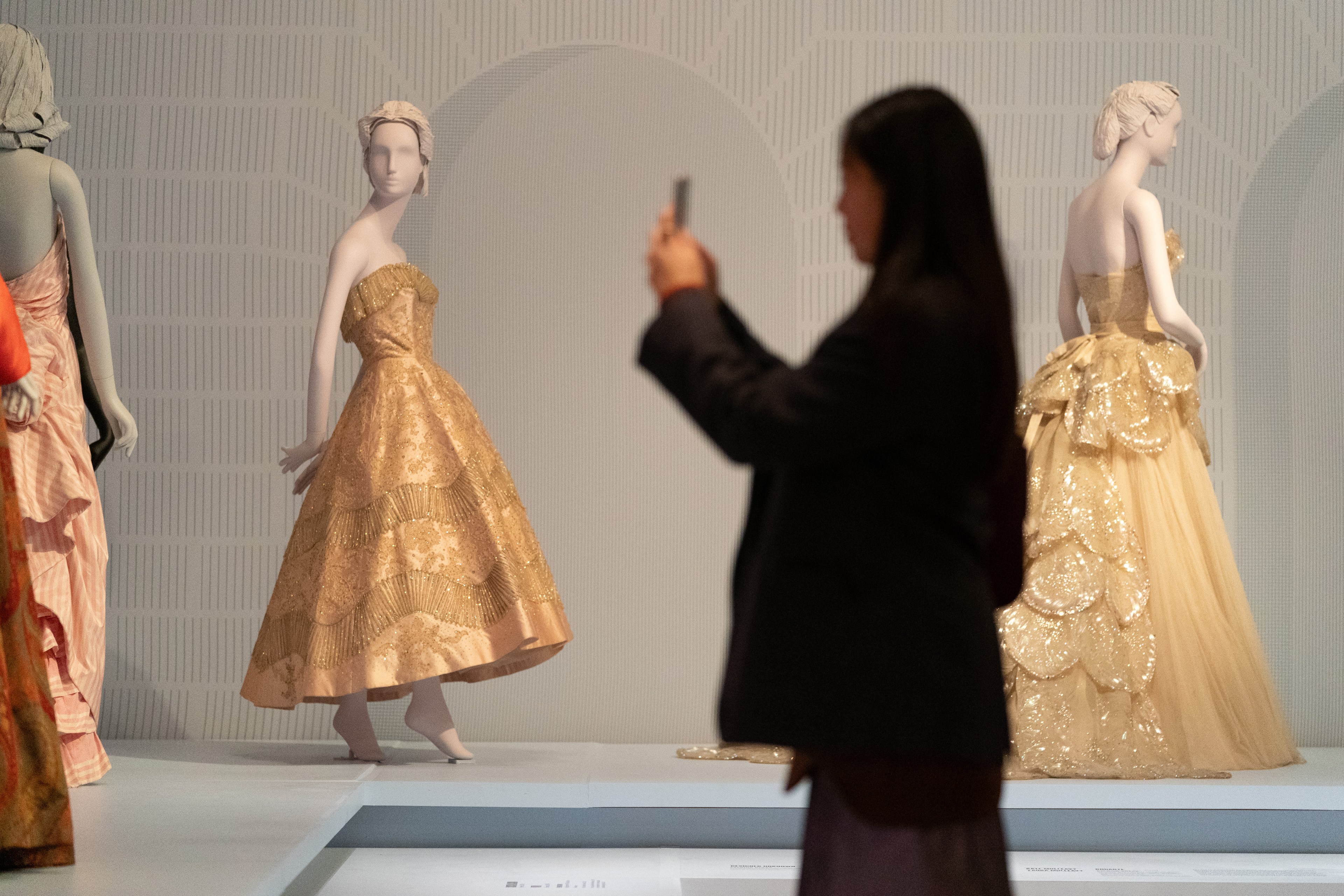 A person in all black takes a photo golden gowns on display.