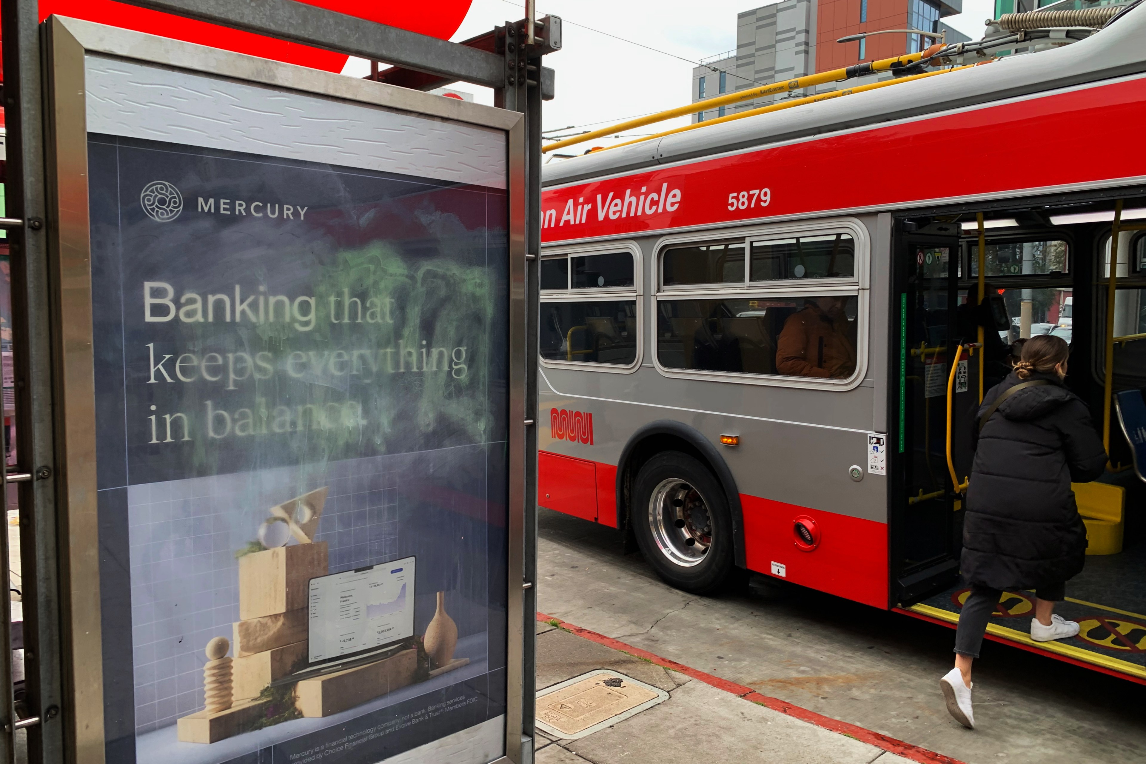 A bus stop ad for Mercury Banking next to a red and silver bus with a person boarding.