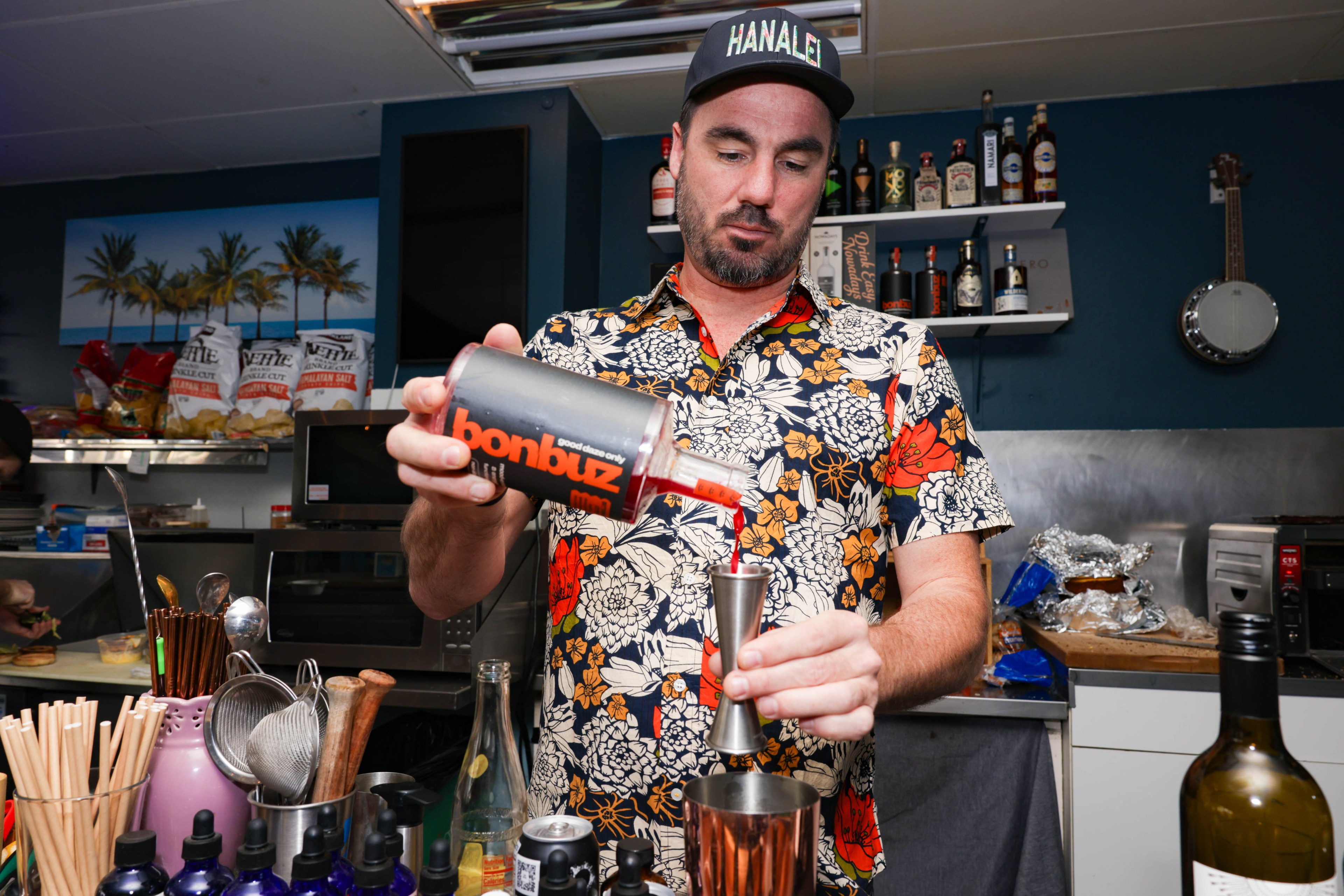 a white male bartender in a Hawaiian shirt mixes a drink