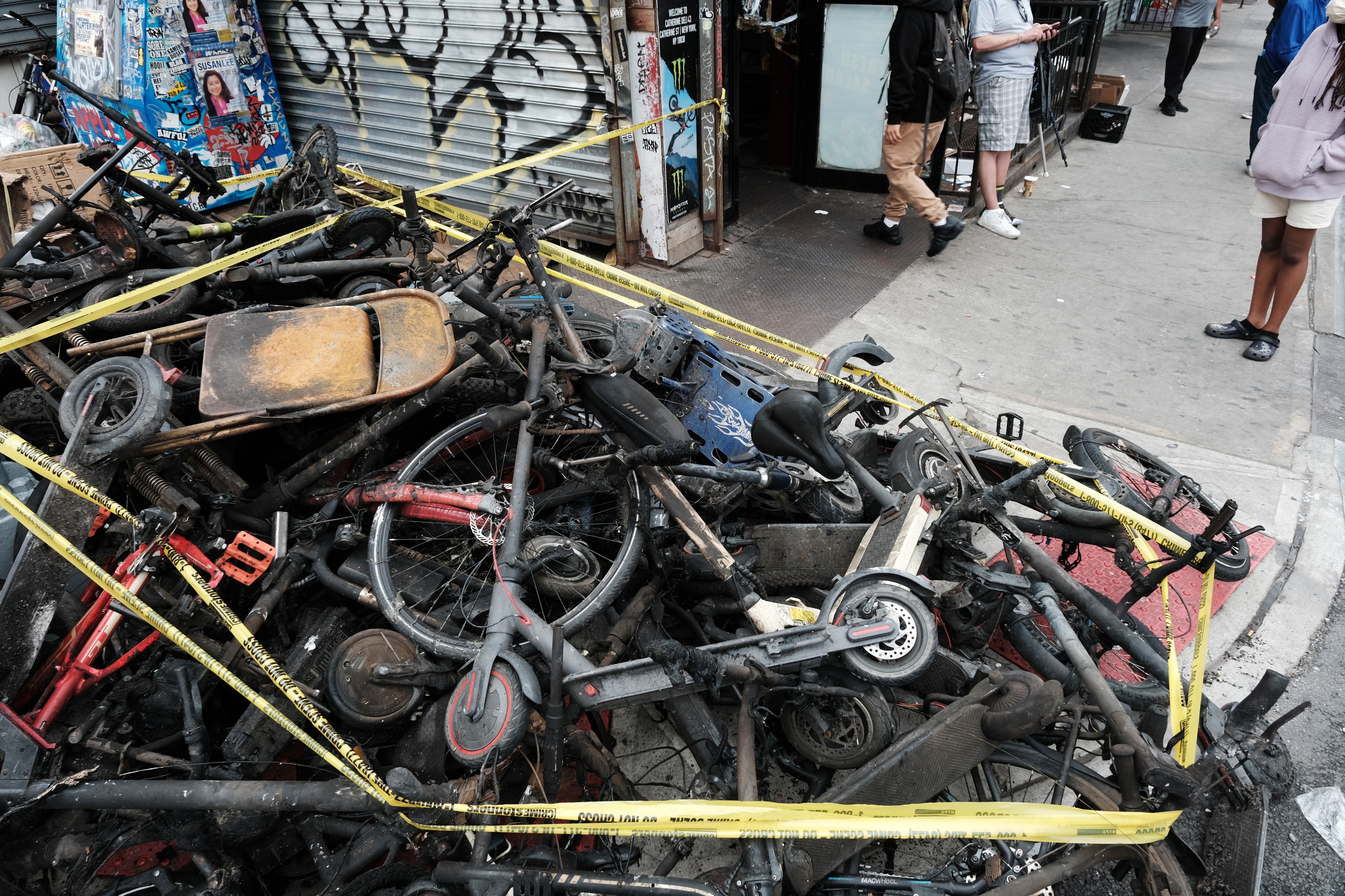 Charred e-scooters and e-bikes stacked in a pile.