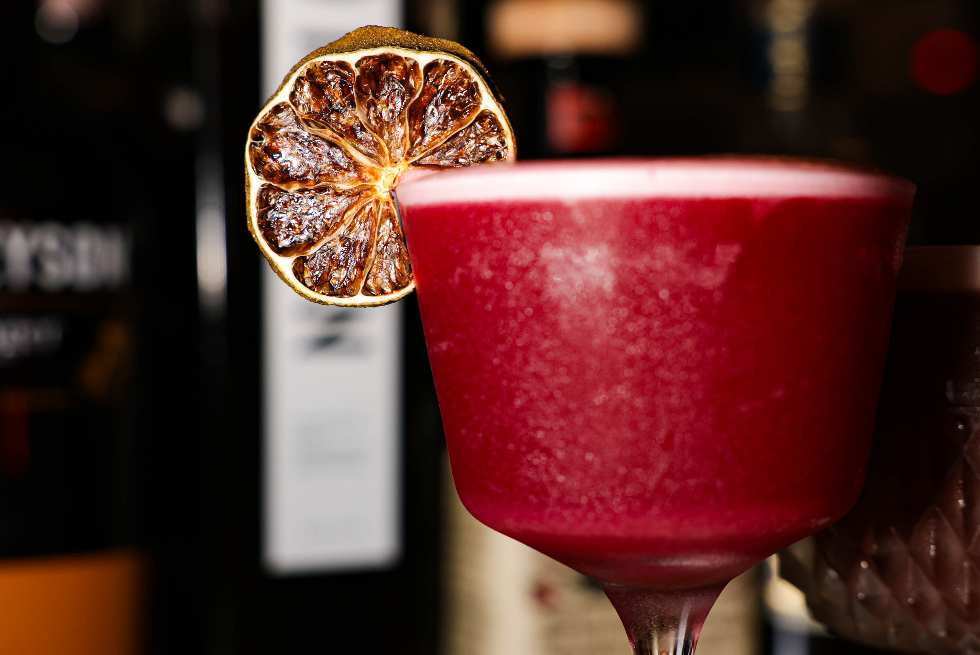 a close-up shot of a purple cocktail garnished with a lime wheel