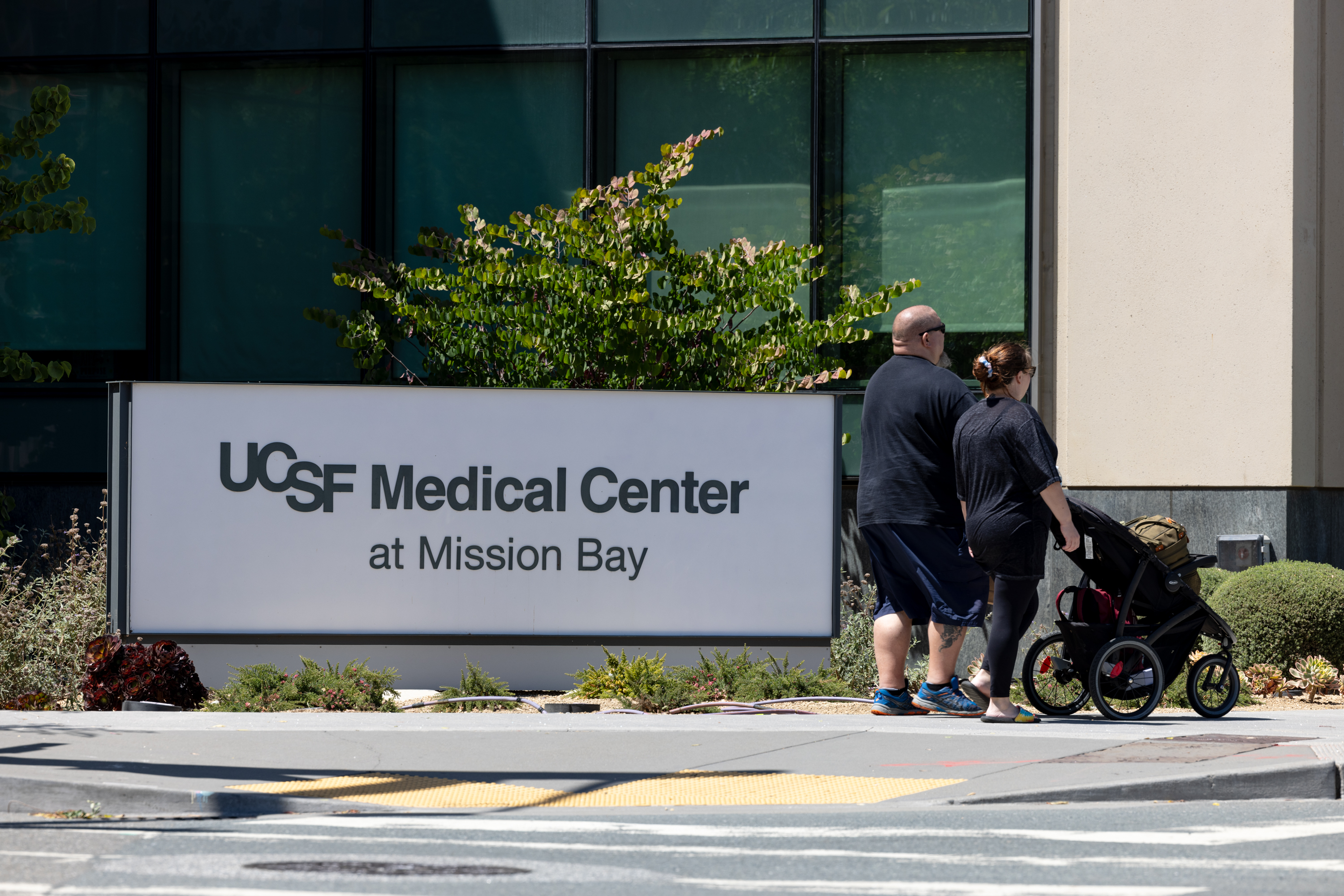 Man and woman walk down sidewalk with stroller outside hospital building