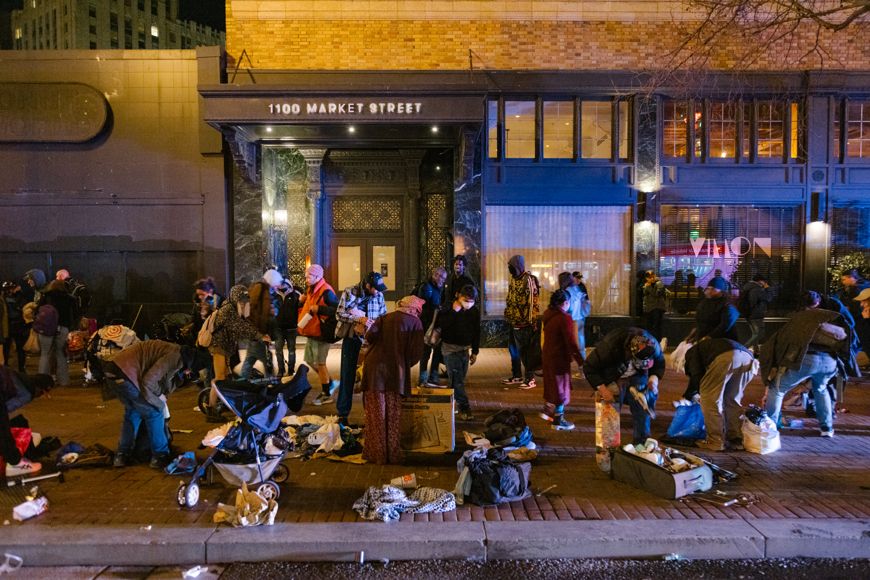 People rummaging through scattered items on a sidewalk at night, in front of a building labeled &quot;1100 Market Street.&quot;