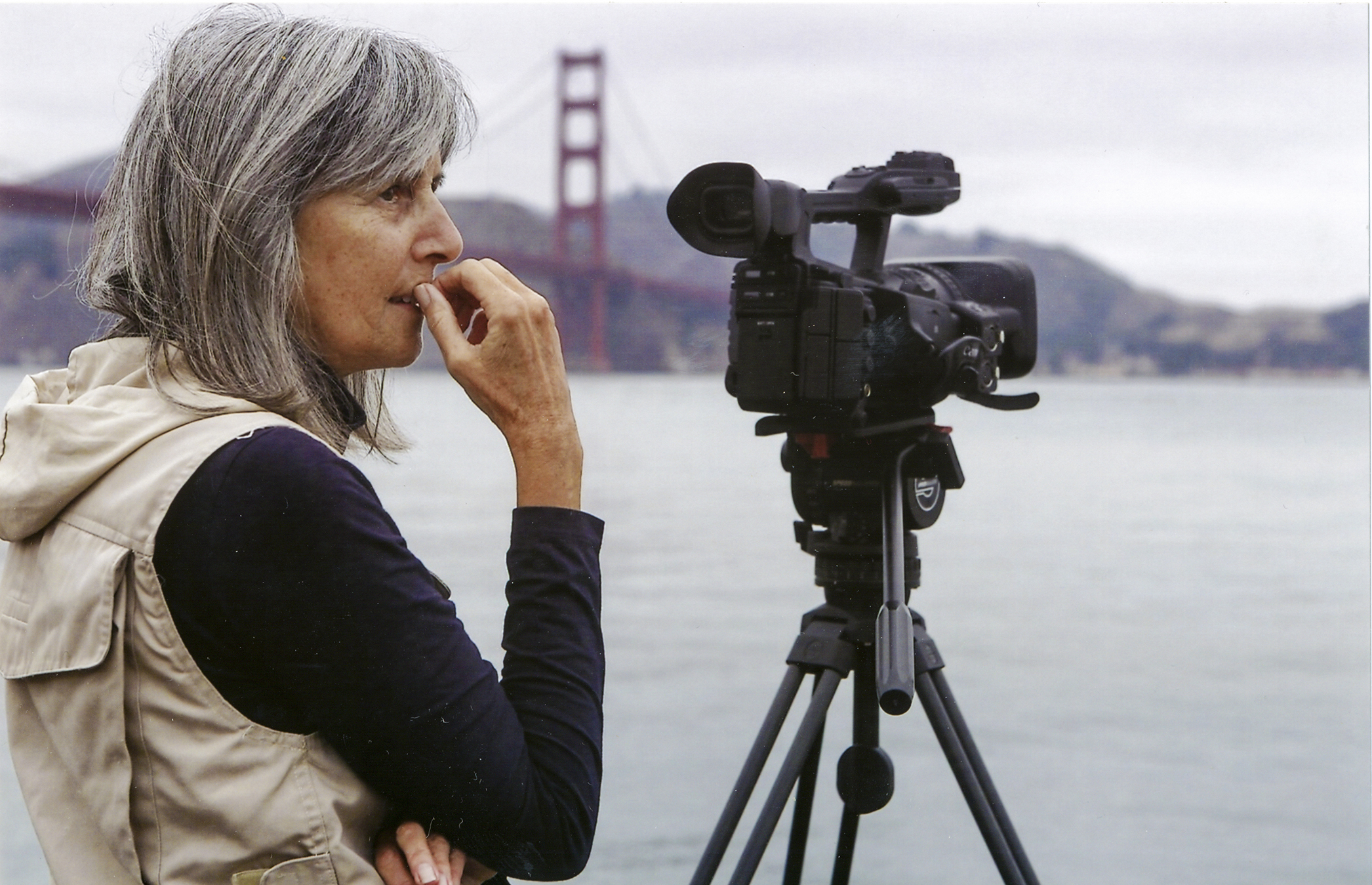 A woman stands beside a movie camera with the Golden Gate Bridge and San Francisco Bay behind her.
