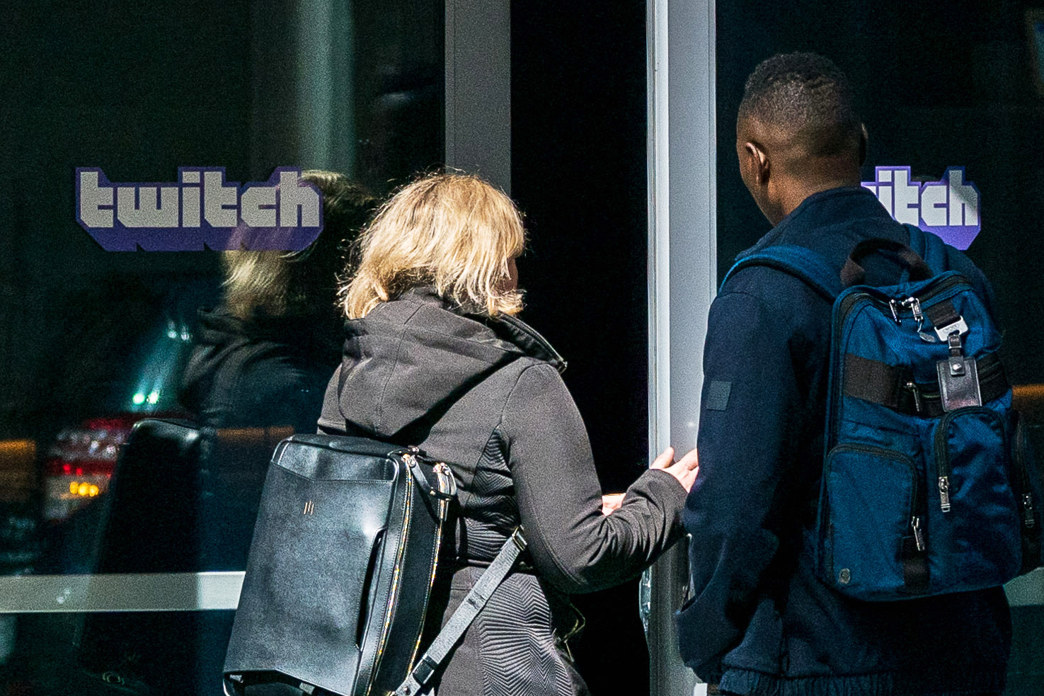 Two people are entering a building with a "Twitch" logo on the door.