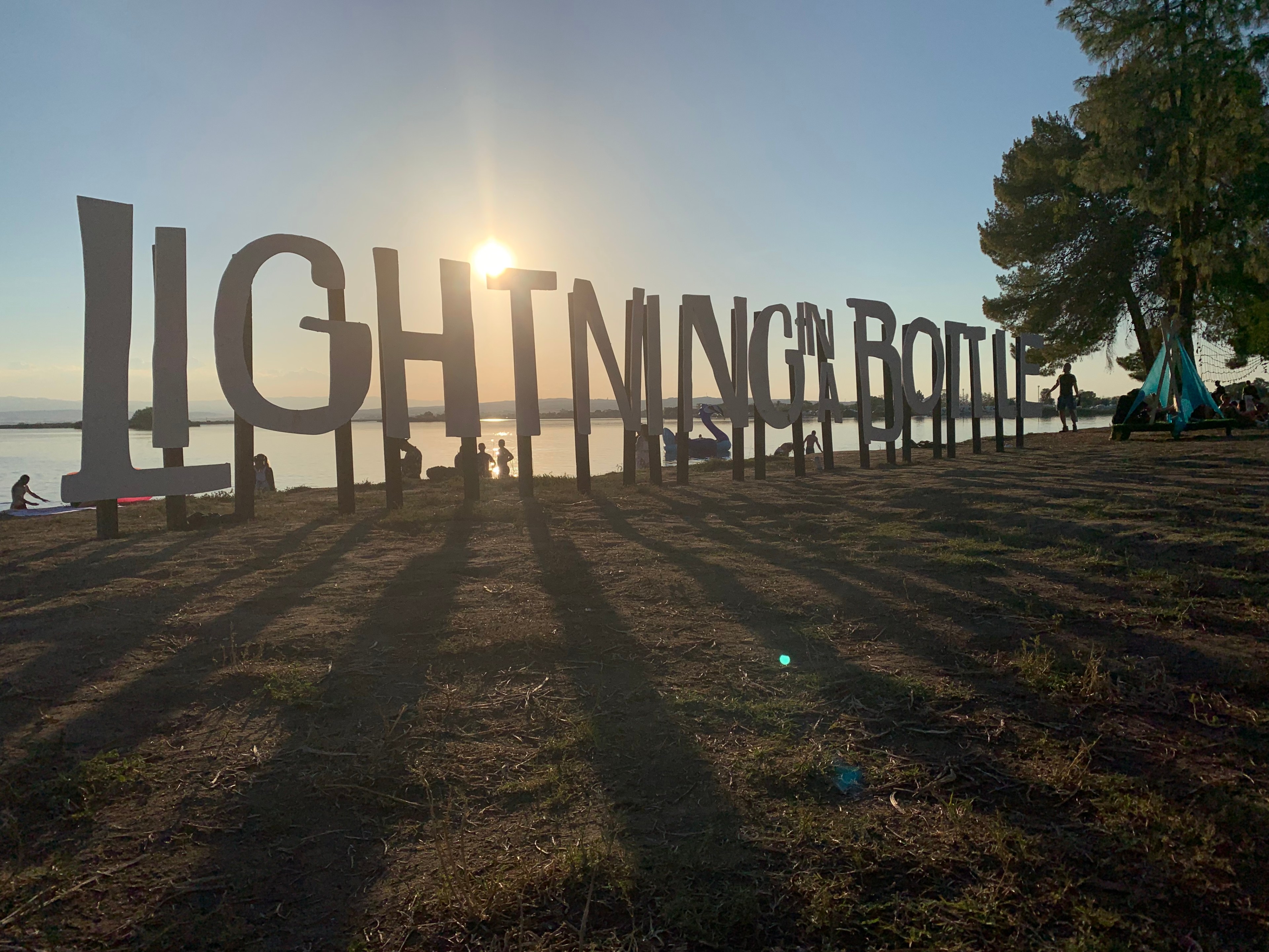 Lightning in a Bottle festival lettering with sun behind on a lake
