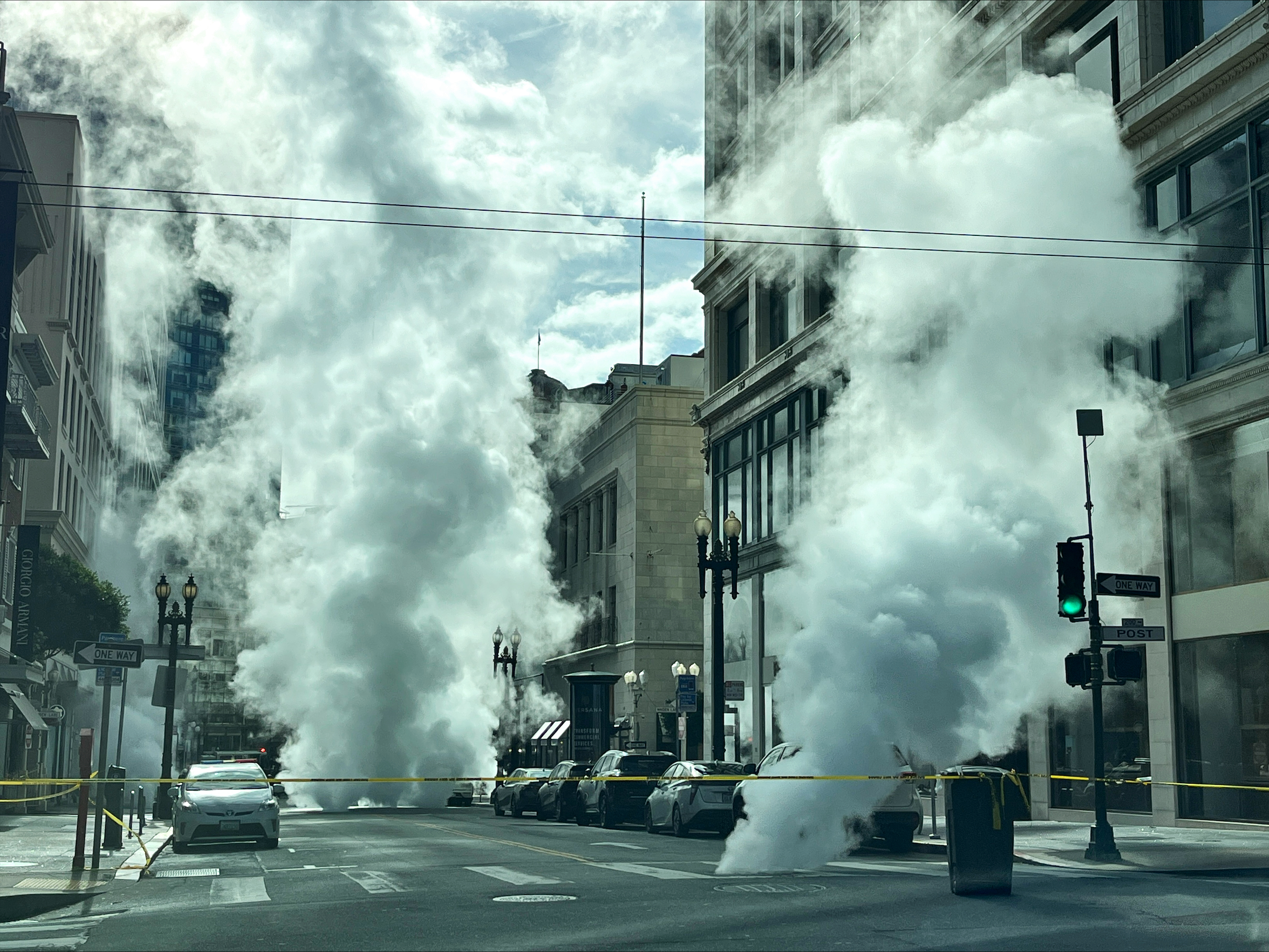 Clouds of steam rise from manholes in a stretch of a downtown city street.