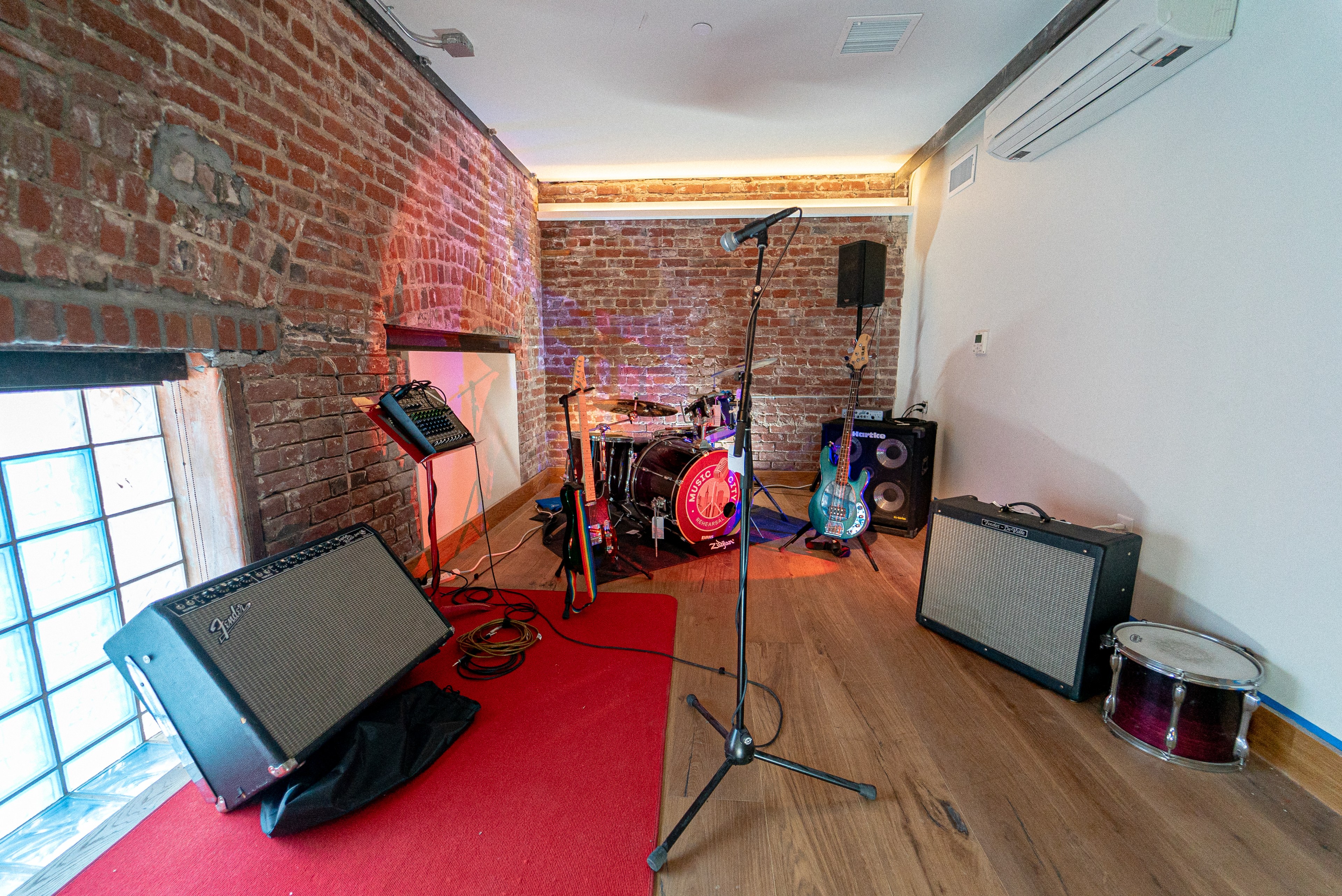 Amps and guitars stand in a room with brick walls and glass windows. 