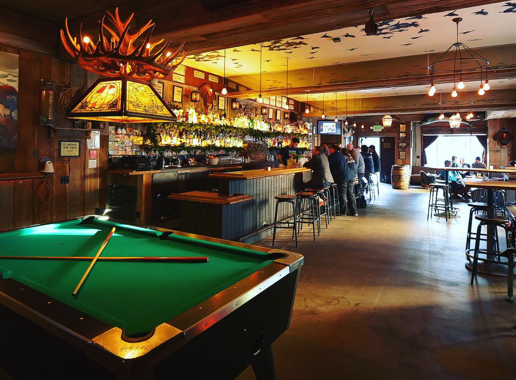 A pool table stands in the foreground of a photo showing a bar.