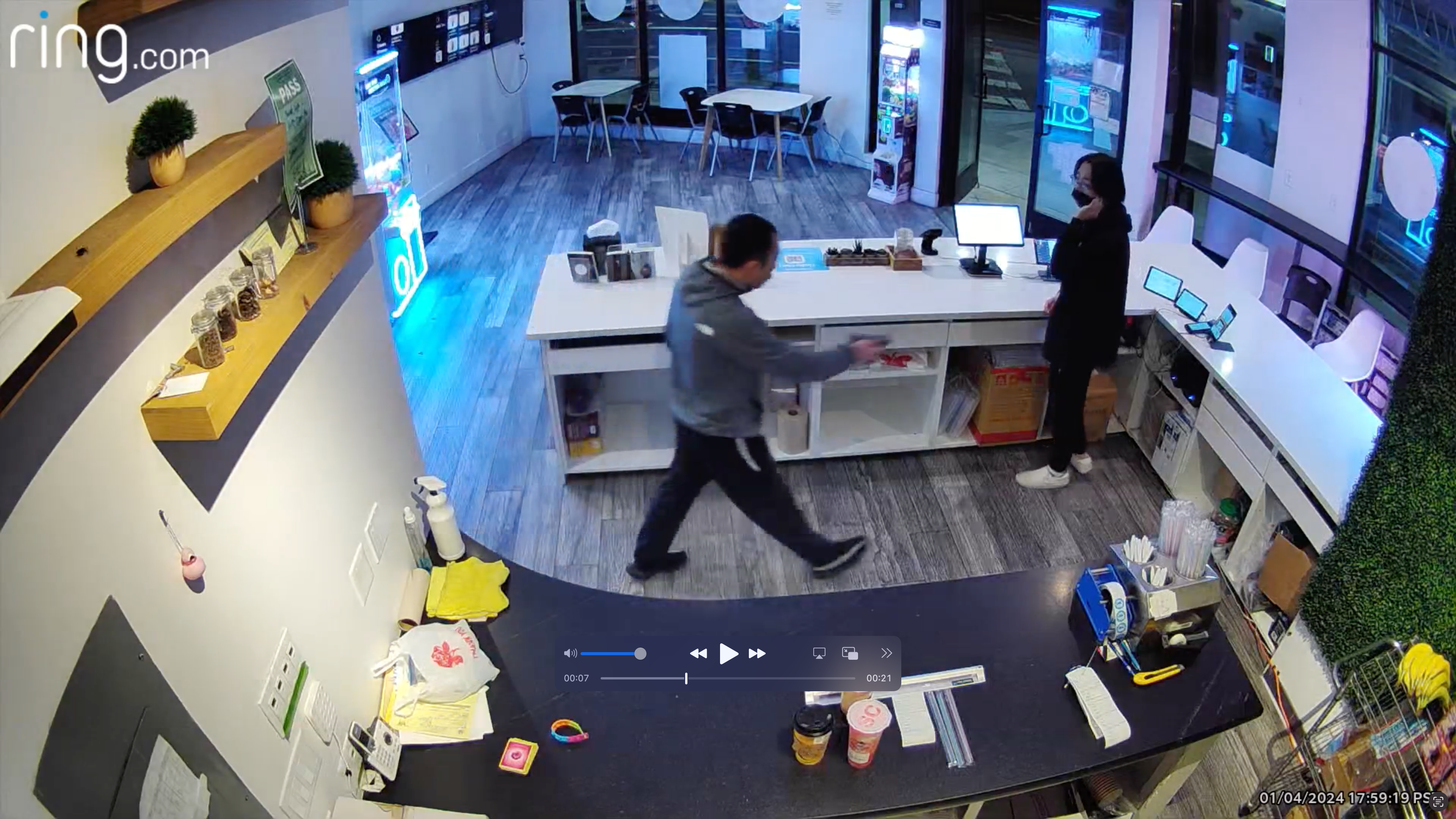 A man with a gun walks behind a counter toward a worker at a cafe.