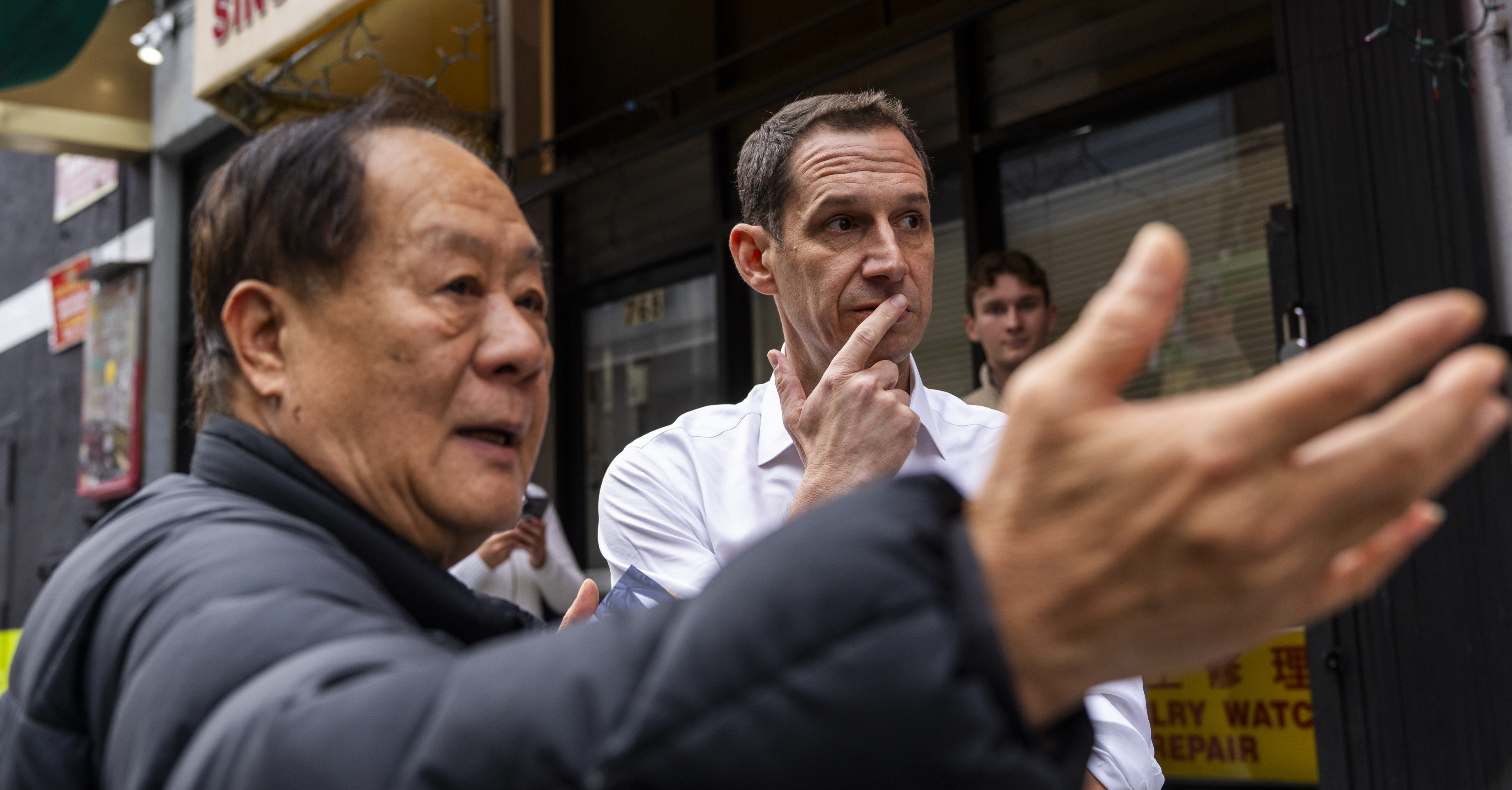 Daniel Lurie talks to an Asian man as they look down the street in San Francisco's Chinatown.