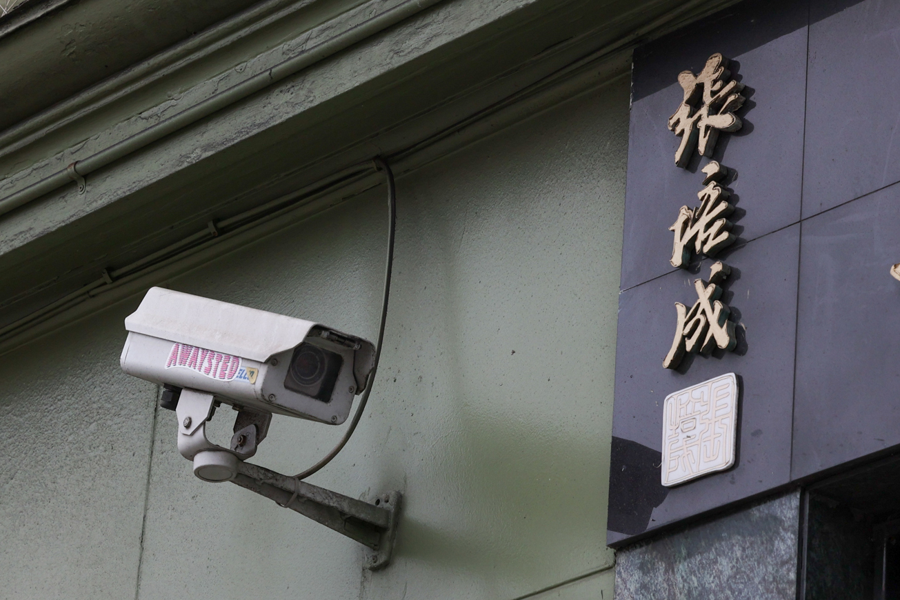 A weathered security camera mounted on a wall next to Asian characters and an emblem.