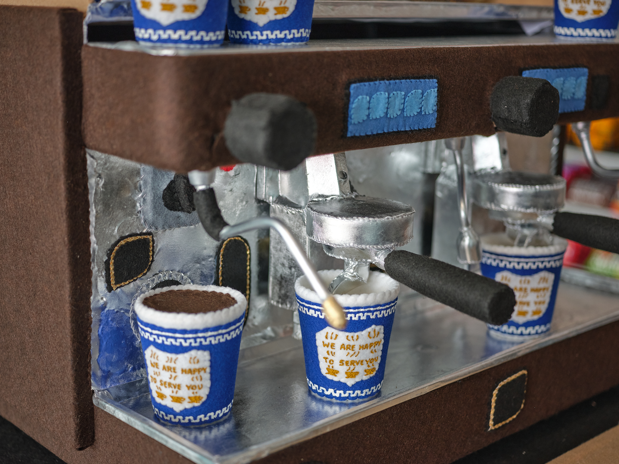 Coffee cups made of felt stand on a fake espresso machine.
