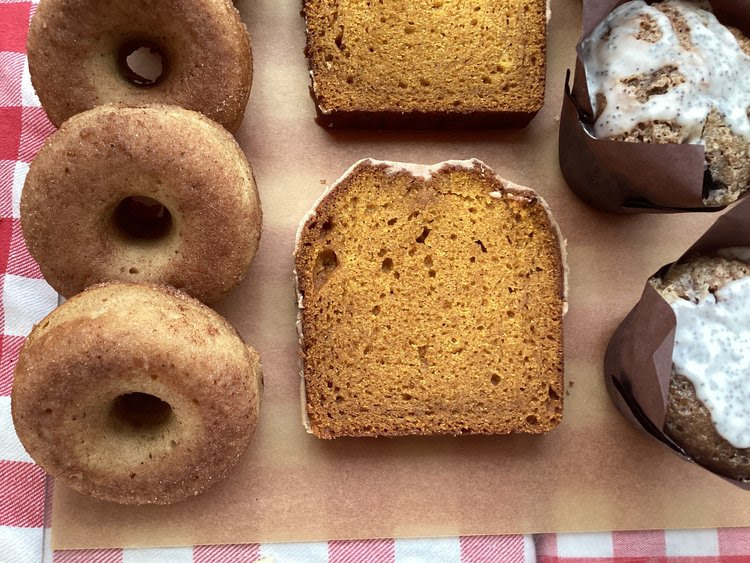 A line of donuts banana bread an muffins stand on tissue paper. 