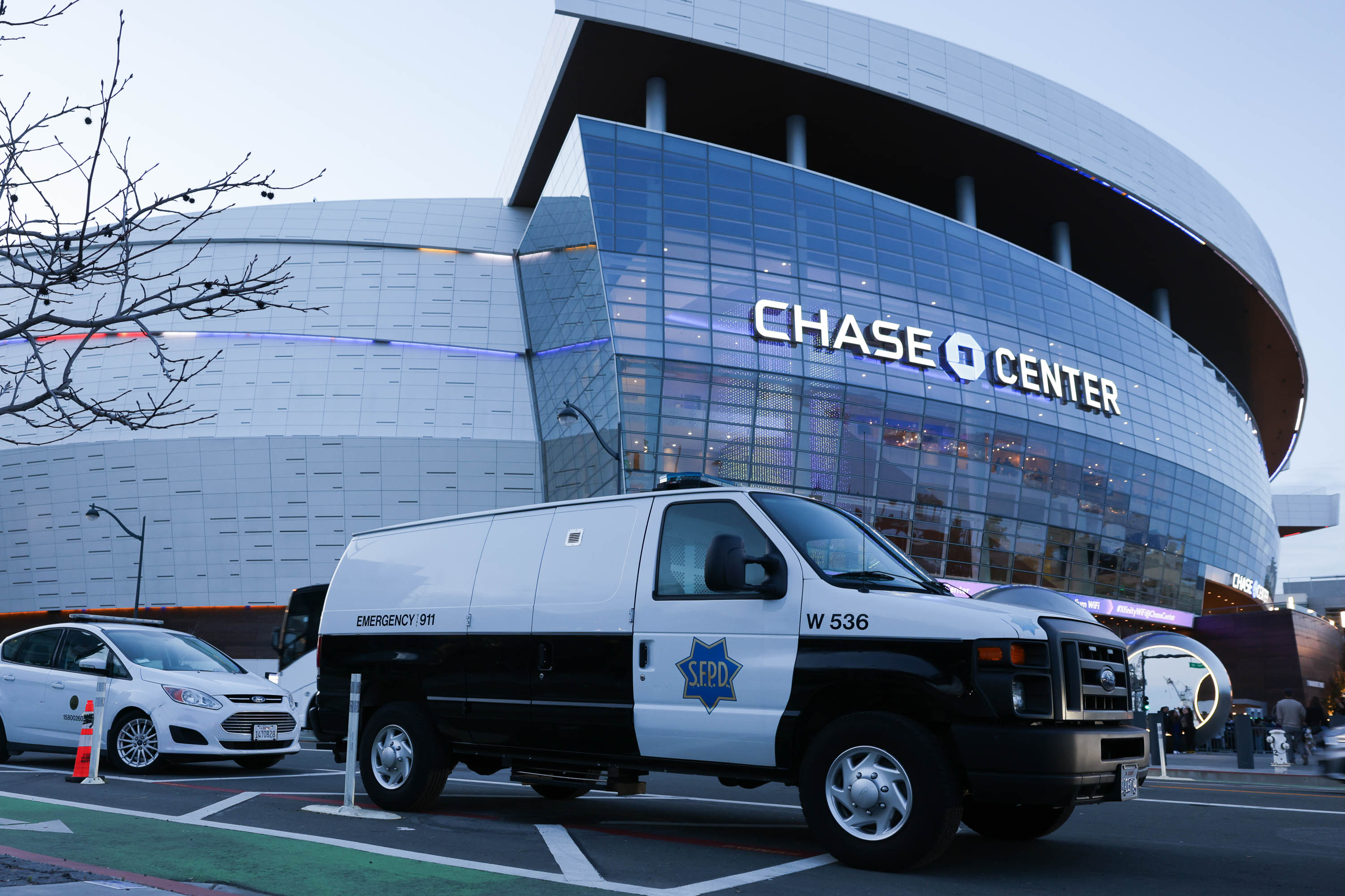 A van labeled &quot;EMERGENCY 911&quot; parks near the illuminated Chase Center arena during dusk.