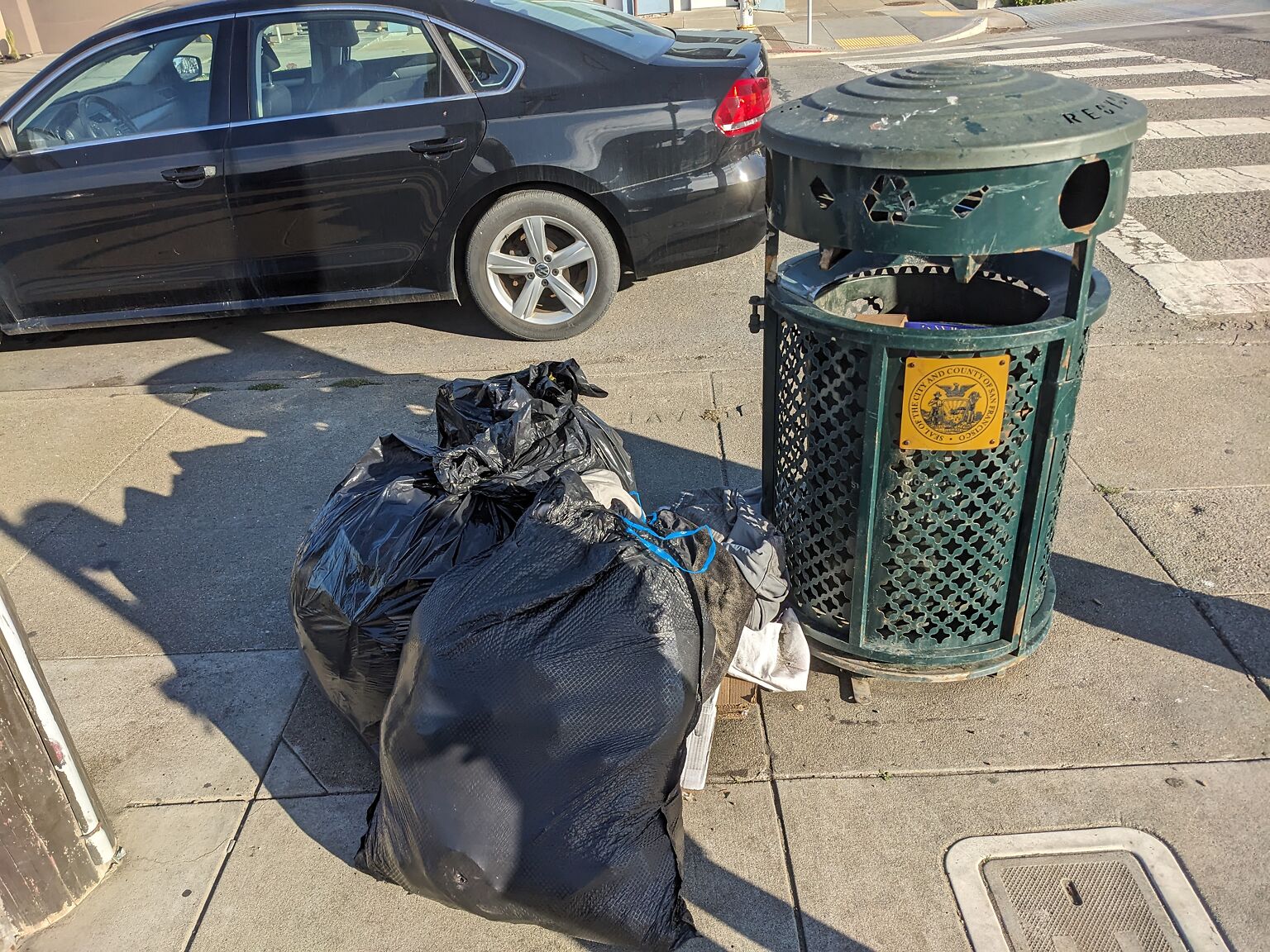Three bags of trash sit next to a San Francisco city trash bin.