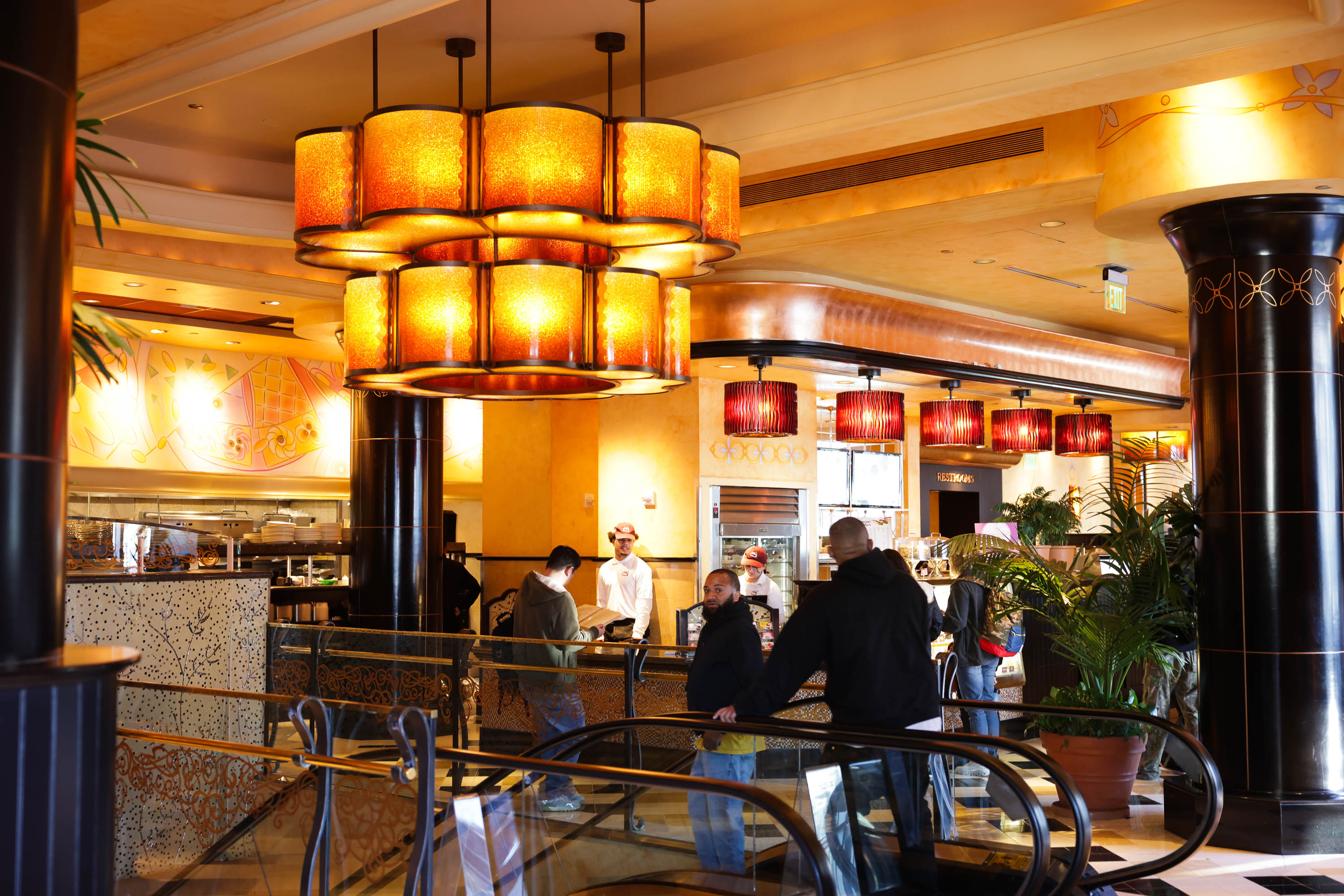 The image shows a warm-lit, upscale restaurant with patrons and chefs, large pendant lamps, and ornate decor.