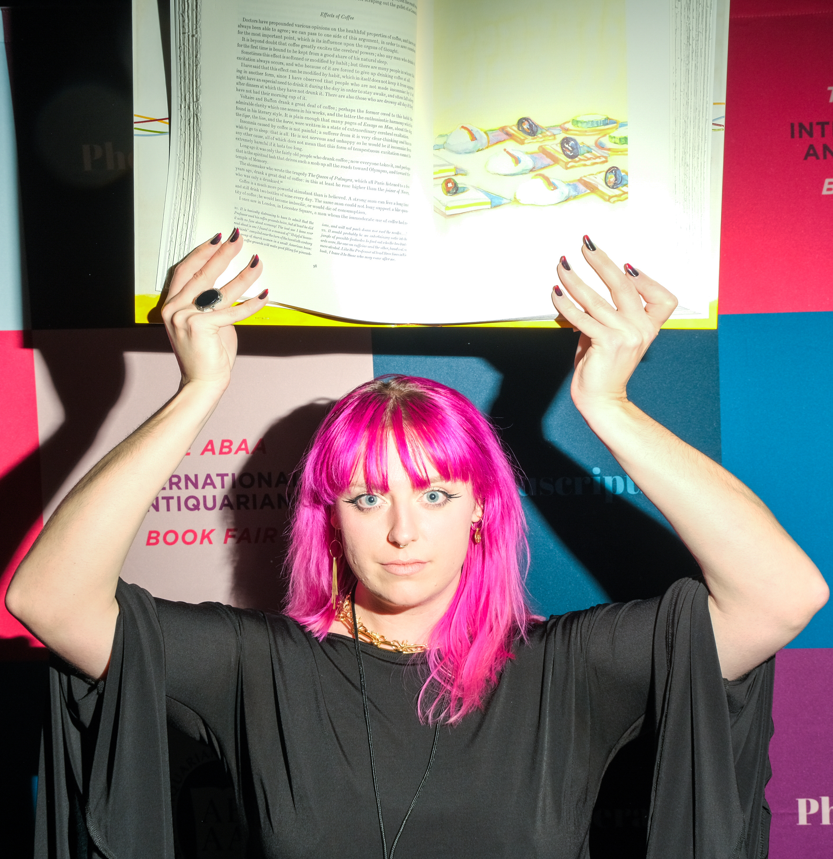 A person with bright pink hair holds open a book on a colorful, abstract background.