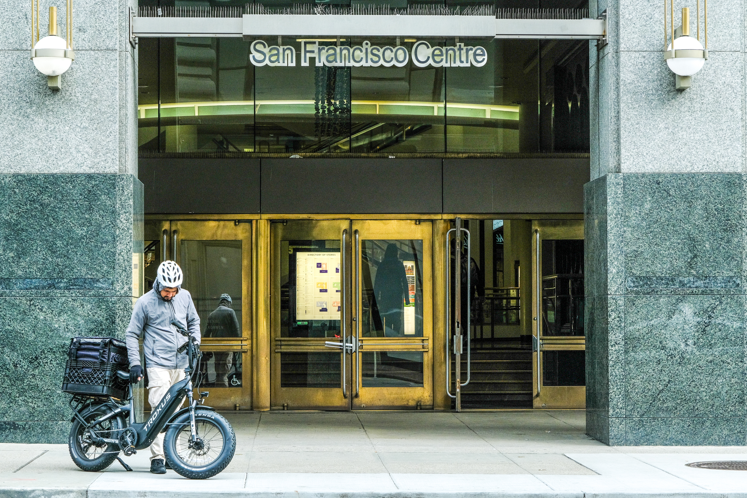 A person by a bike stands in front of the San Francisco Centre entrance with bold signage.