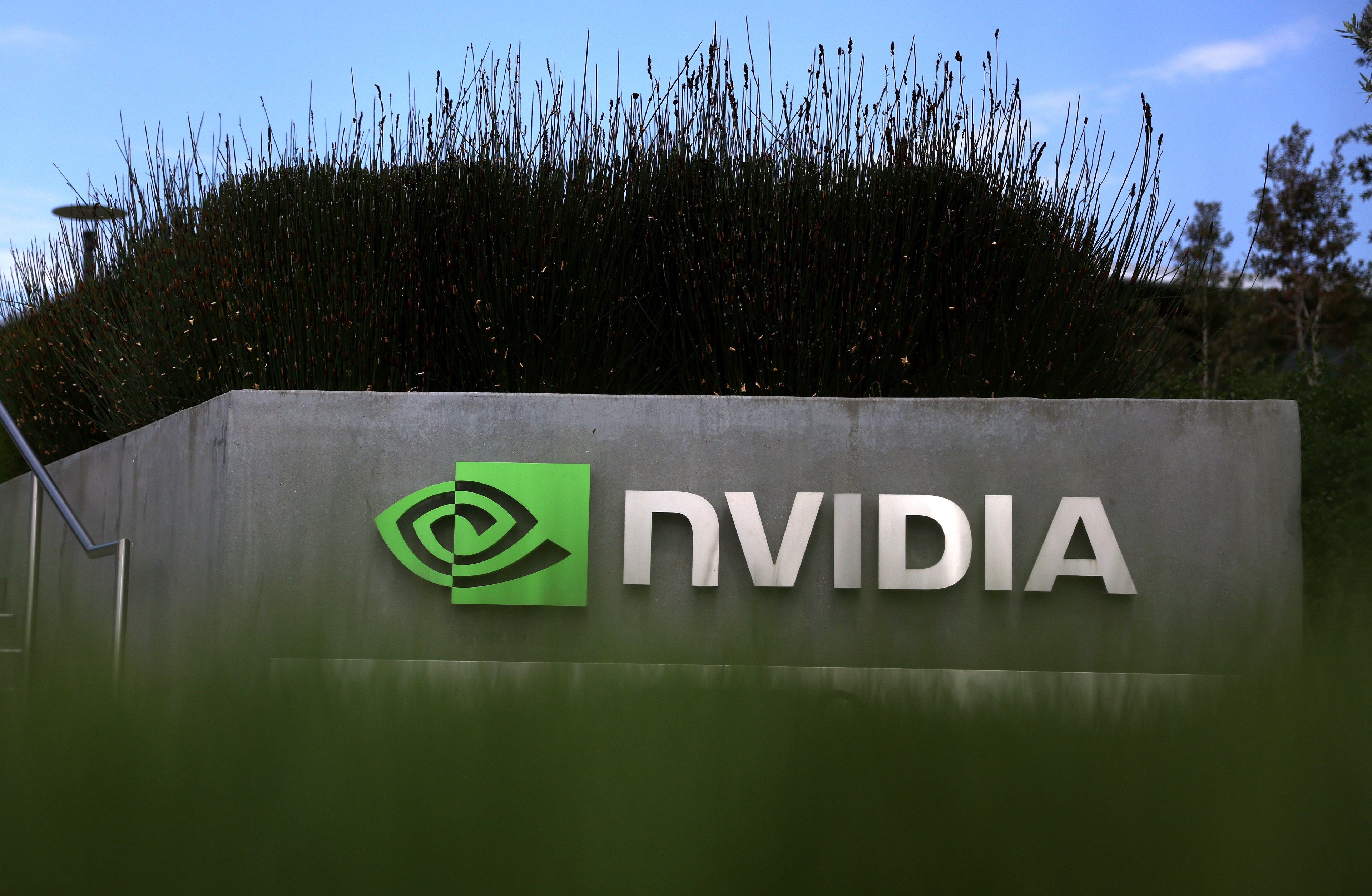 A sign with the NVIDIA logo on a concrete structure, with lush greenery on top and a clear sky behind.