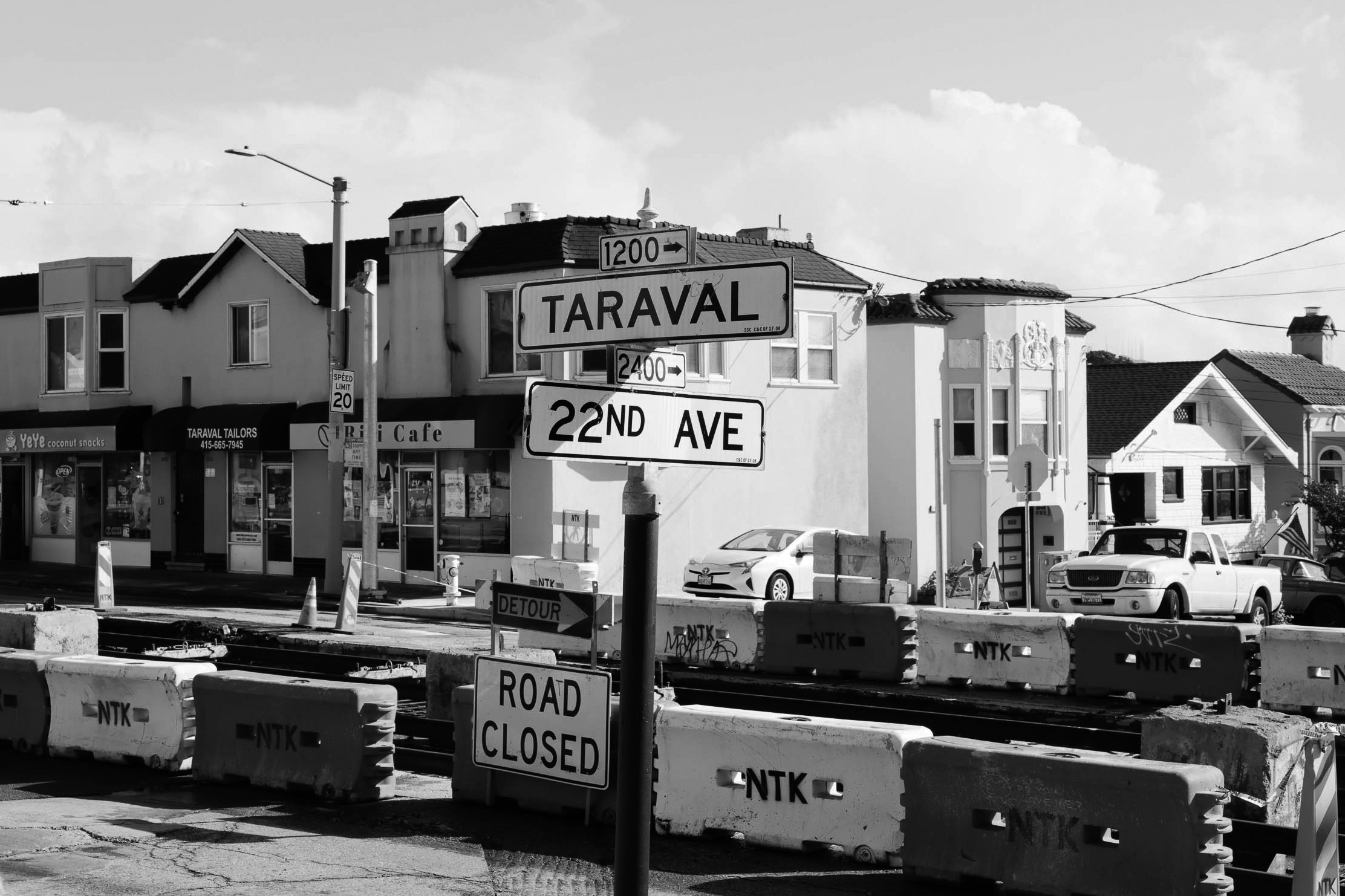 An urban street corner showing roadwork barriers with "ROAD CLOSED" signs, under a street sign for "TARAVAL" and "22ND AVE."