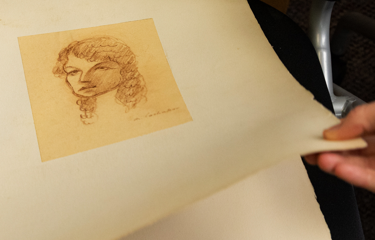 An old drawing of a woman's face on aged paper is being revealed as someone peels back a protective layer.