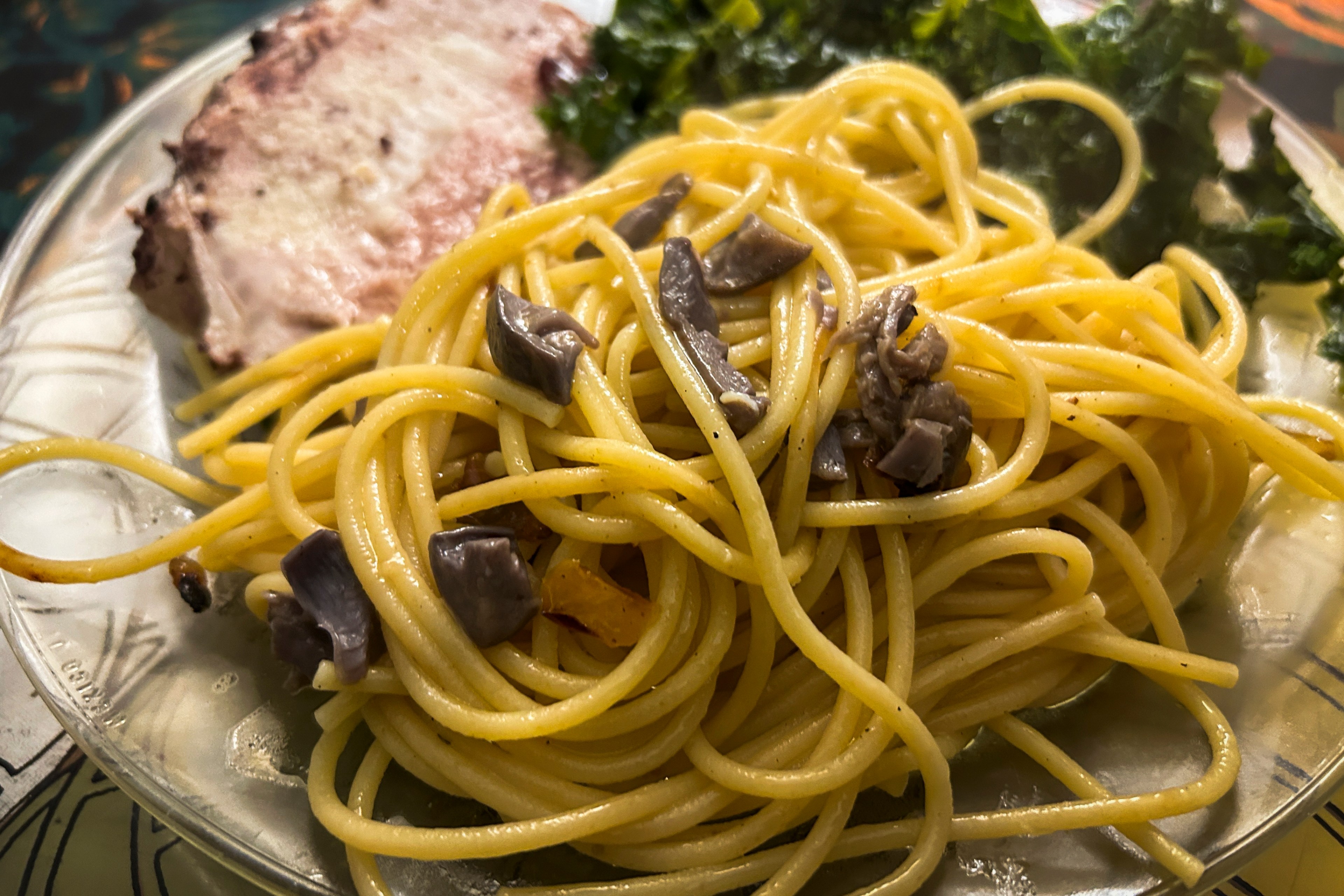 a plate of spaghetti with blewits, and pork loin and kale in the background.
