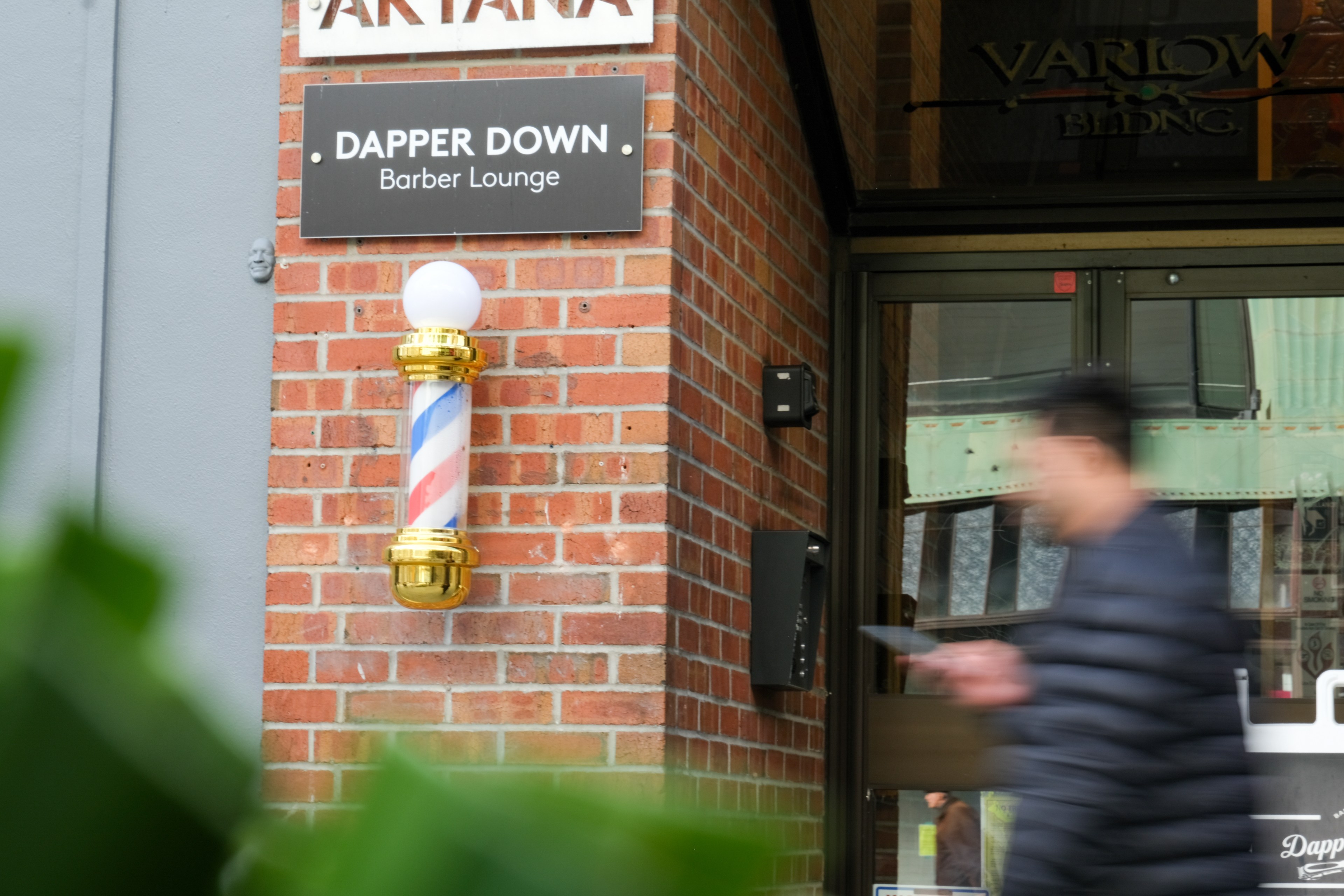 A rotating barber's pole with a blurred person walking by outside a barber lounge.