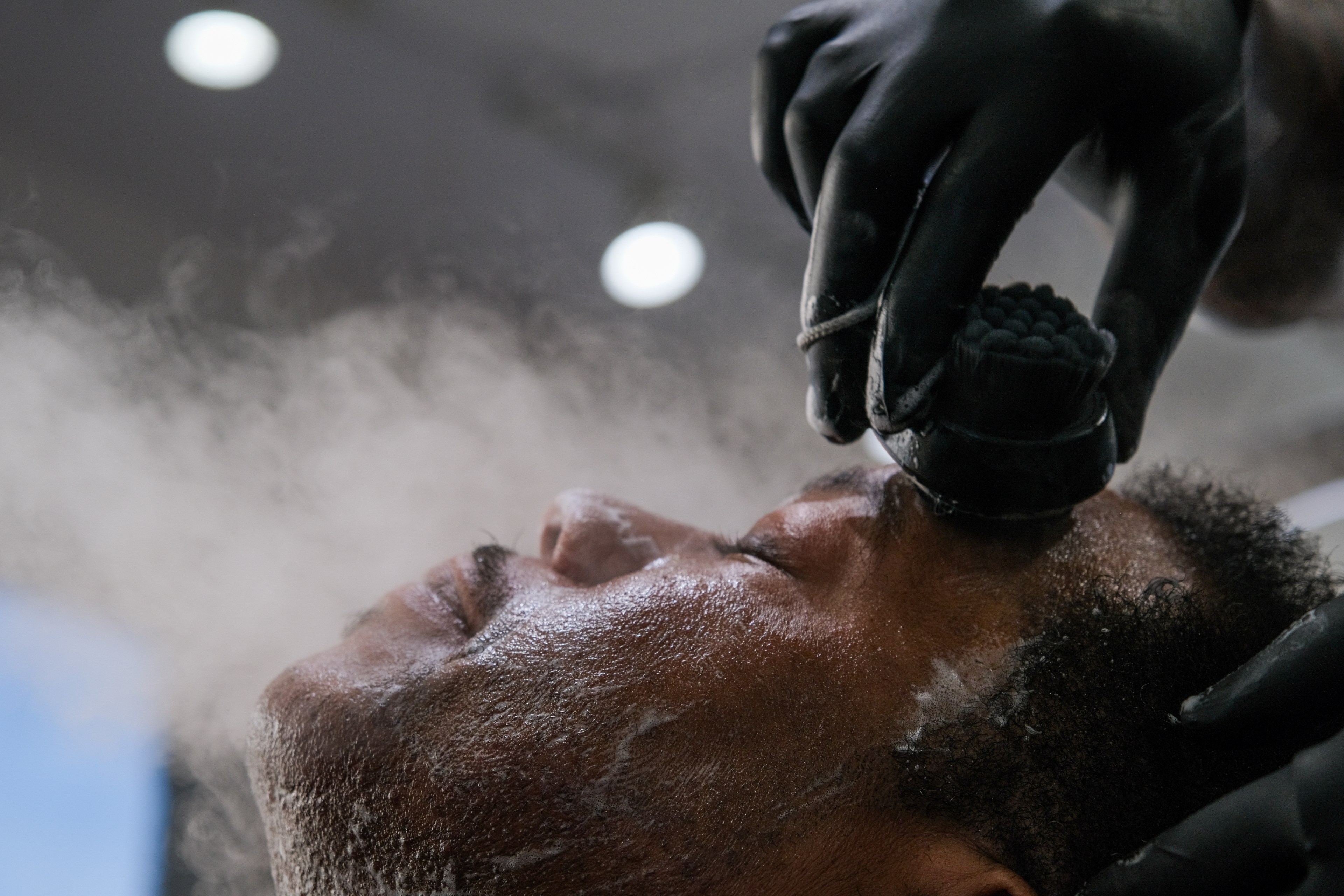 A person receiving a shave; a cloud of talcum powder surrounds their face as the barber works.