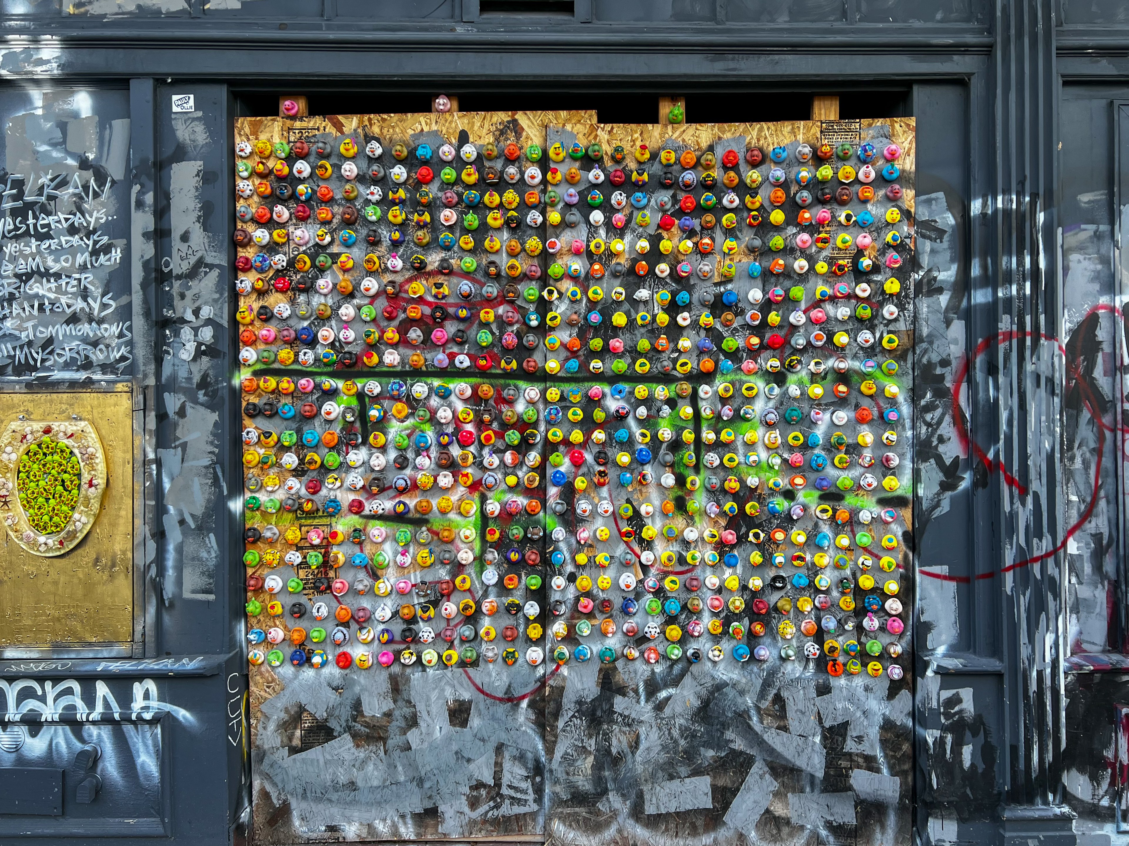 an art piece consisting of 663 mounted rubber ducks on a wall facing a city sidewalk