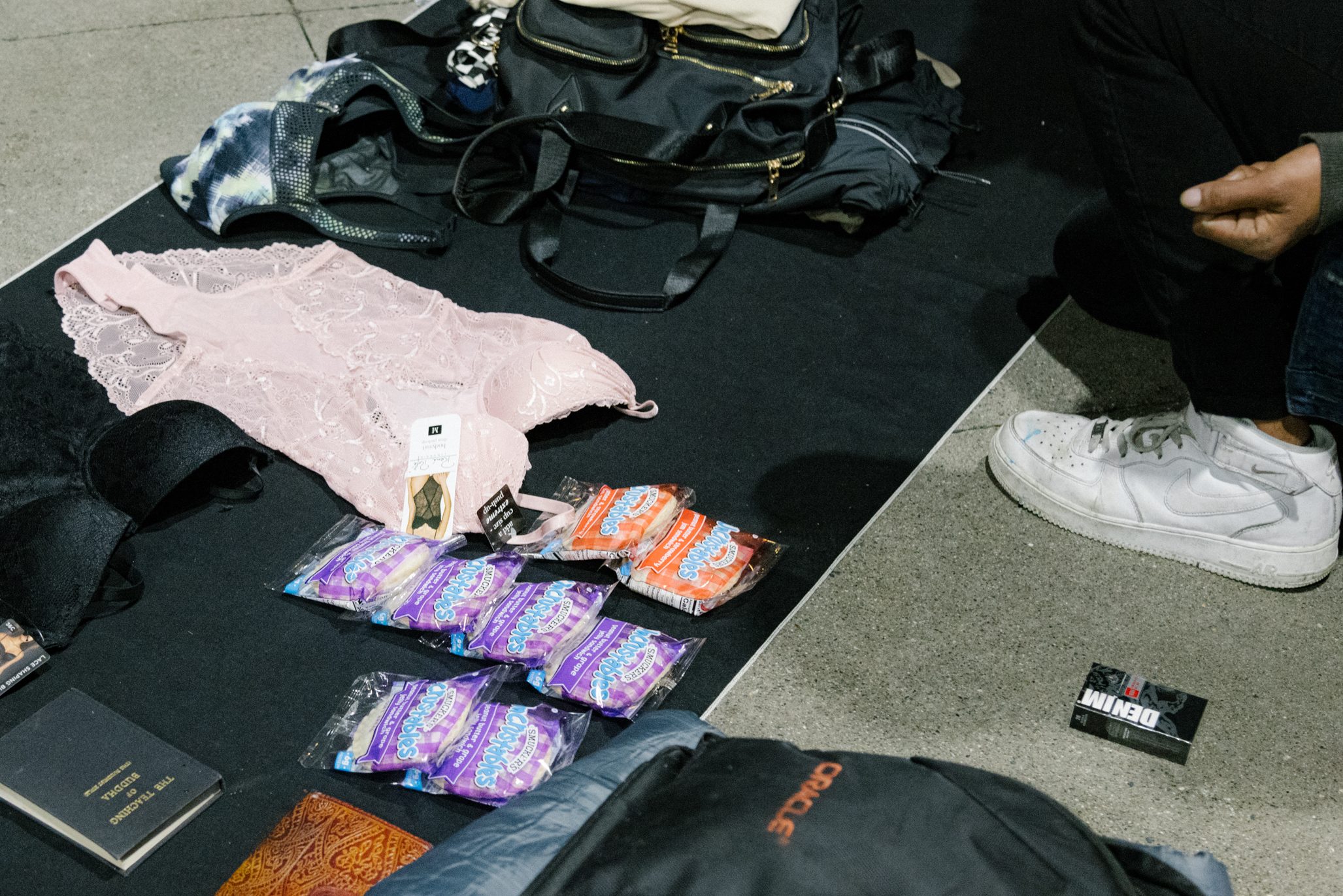 A collection of items on a mat: clothing, bags, and packets, with a person seated at the edge.