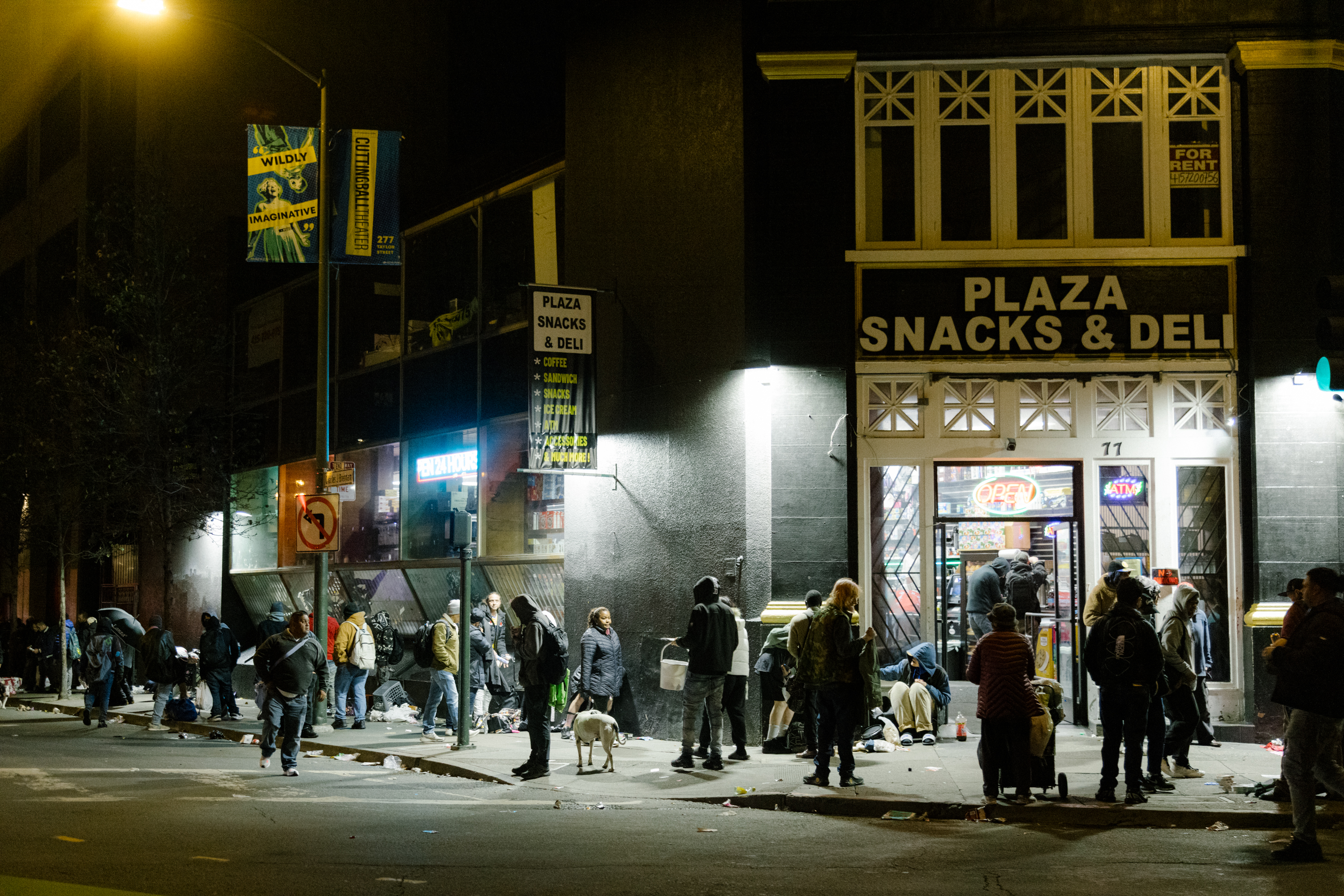 A nighttime scene with people gathering outside "Plaza Snacks & Deli," some with dogs, amid a lit "OPEN" sign.