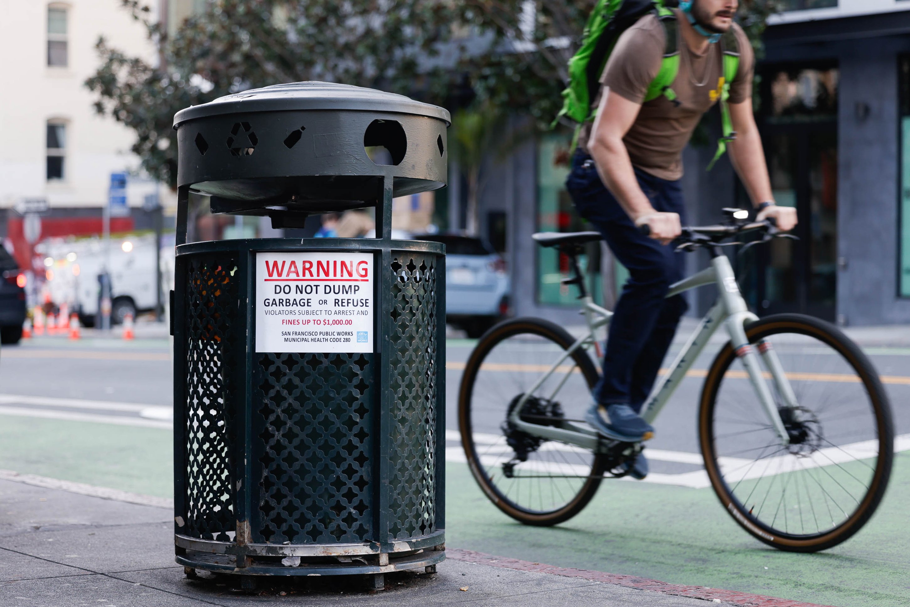 A bicyclist rides by a trash can marked with a sign that reads: "Warning: Do not dump garbage or refuse."