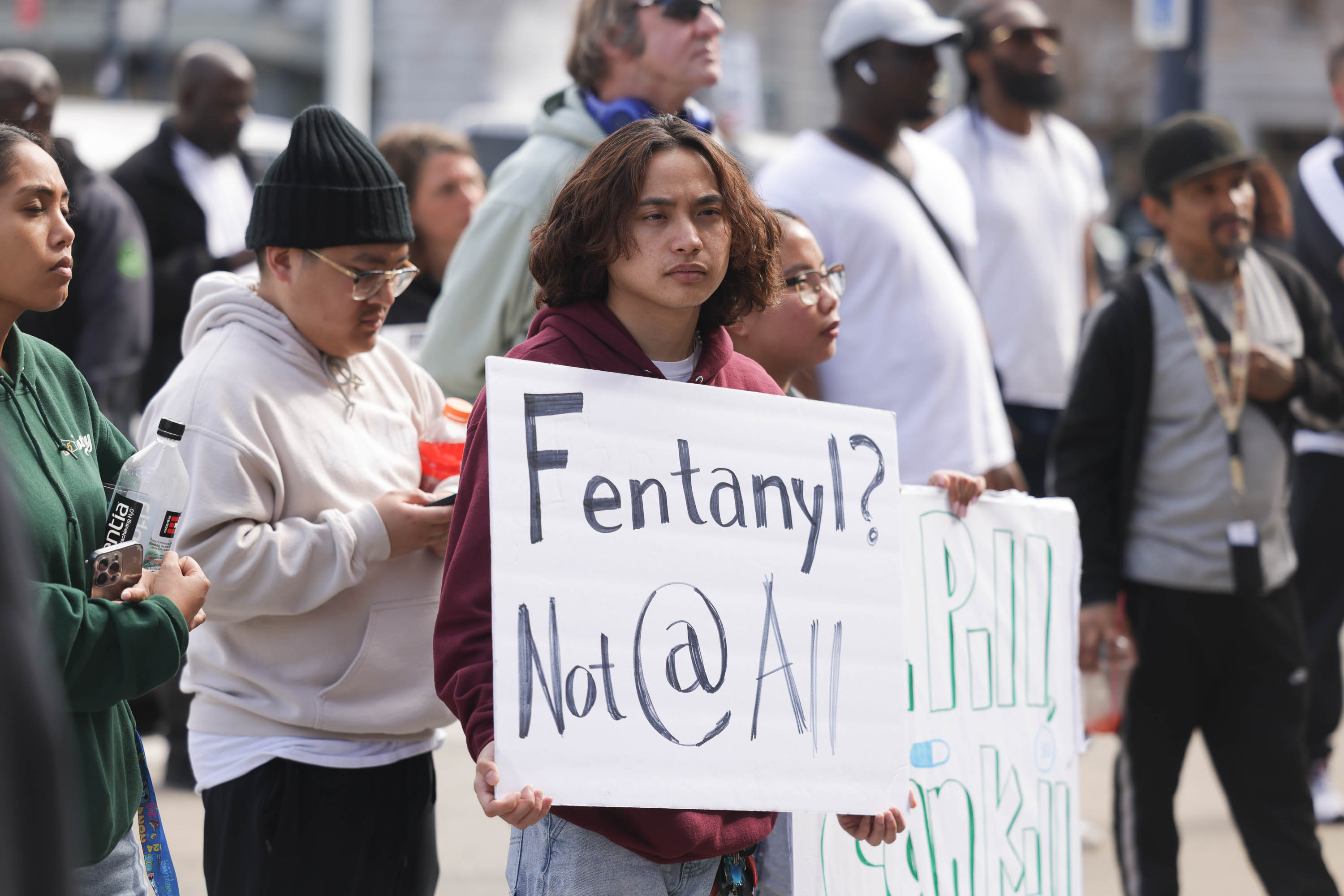 A person is holding a sign reading &quot;Fentanyl? Not @ All&quot; in a crowd.
