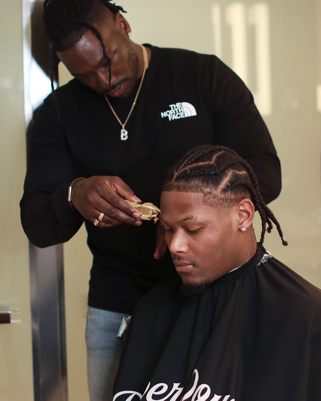 A barber, focused and using clippers, is meticulously shaping another man's hair.