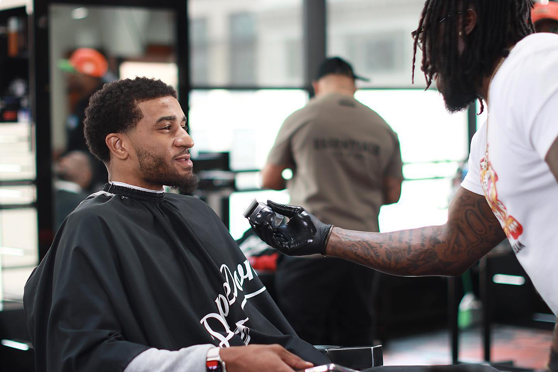 A barber with tattoos is giving a haircut to a smiling man in a salon.