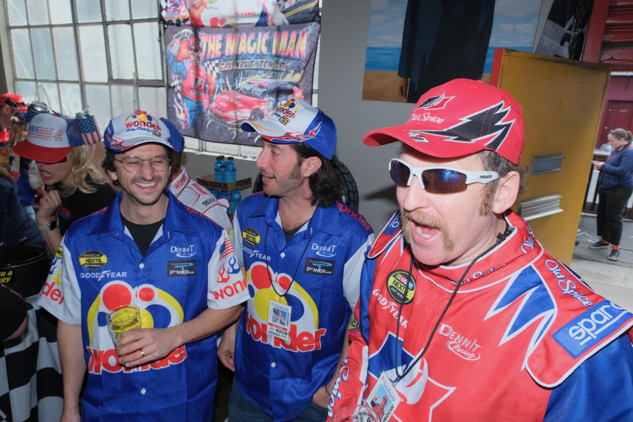 Three men in racing uniforms and caps, with a NASCAR theme, are enjoying a lively moment together.