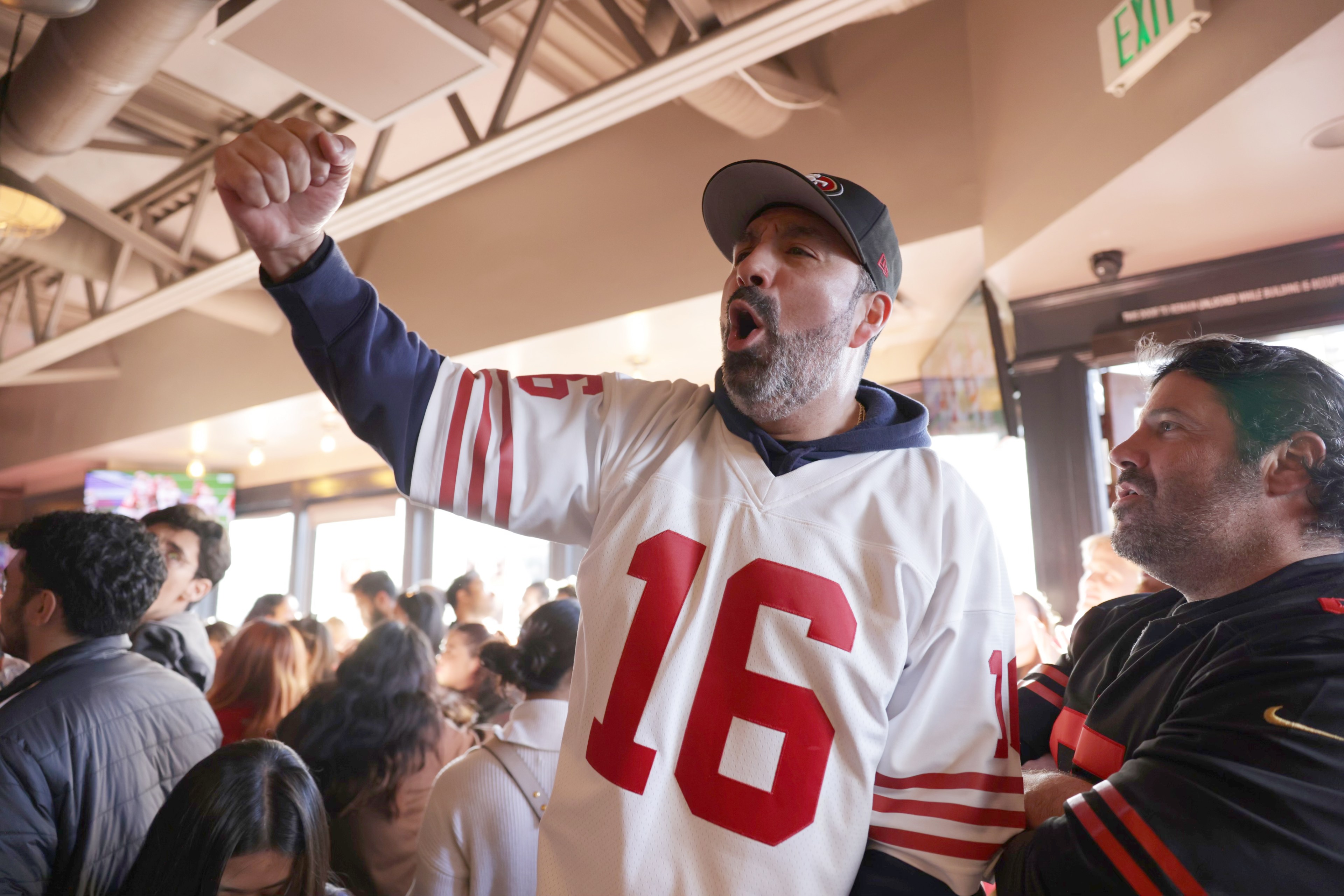 Man in white 49ers jersey raises fist and cheers