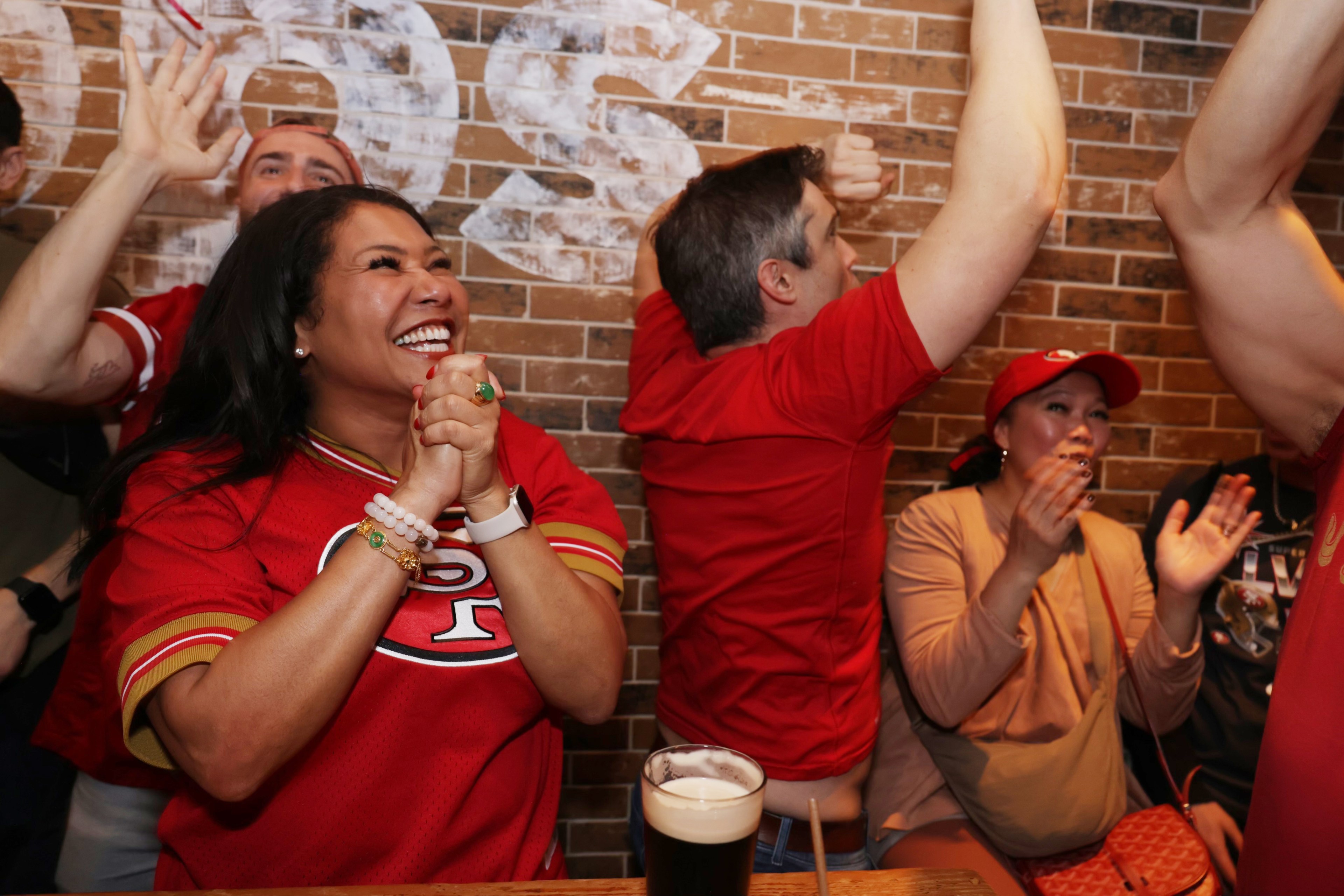 A group of fans in red jerseys celebrates joyously in a bar.